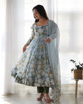 Woman wearing a floral dress with a light blue dupatta in a bright room.
