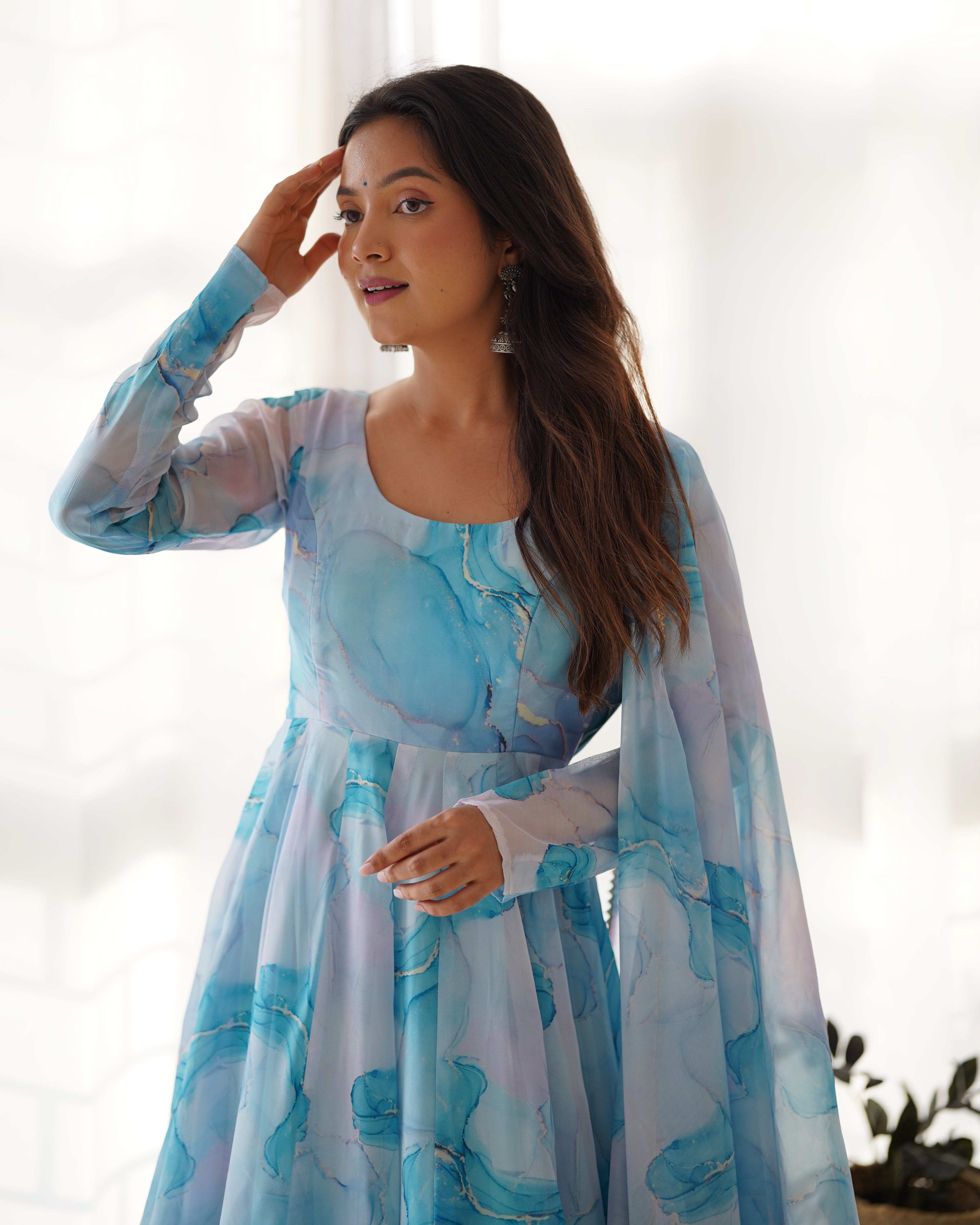 Woman wearing a light blue and white floral dress with a sheer overlay against a blurred background