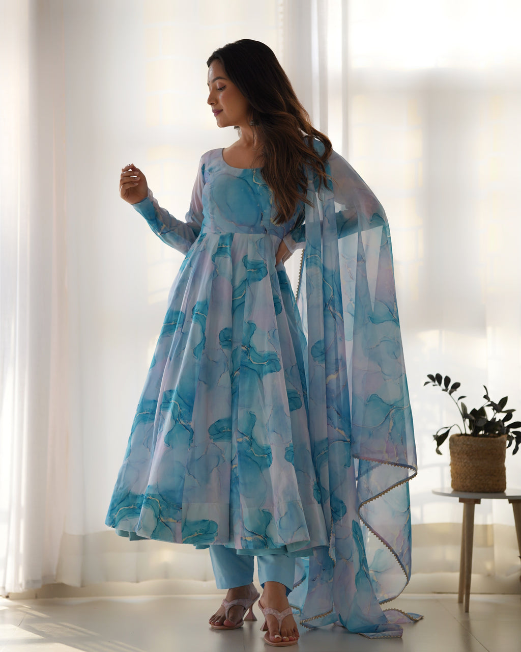 Woman wearing a blue floral dress with a sheer dupatta in a bright room.