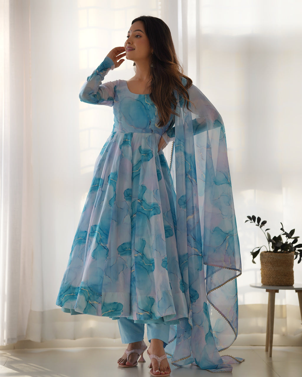 Woman wearing a blue floral dress with a matching dupatta in a bright room.