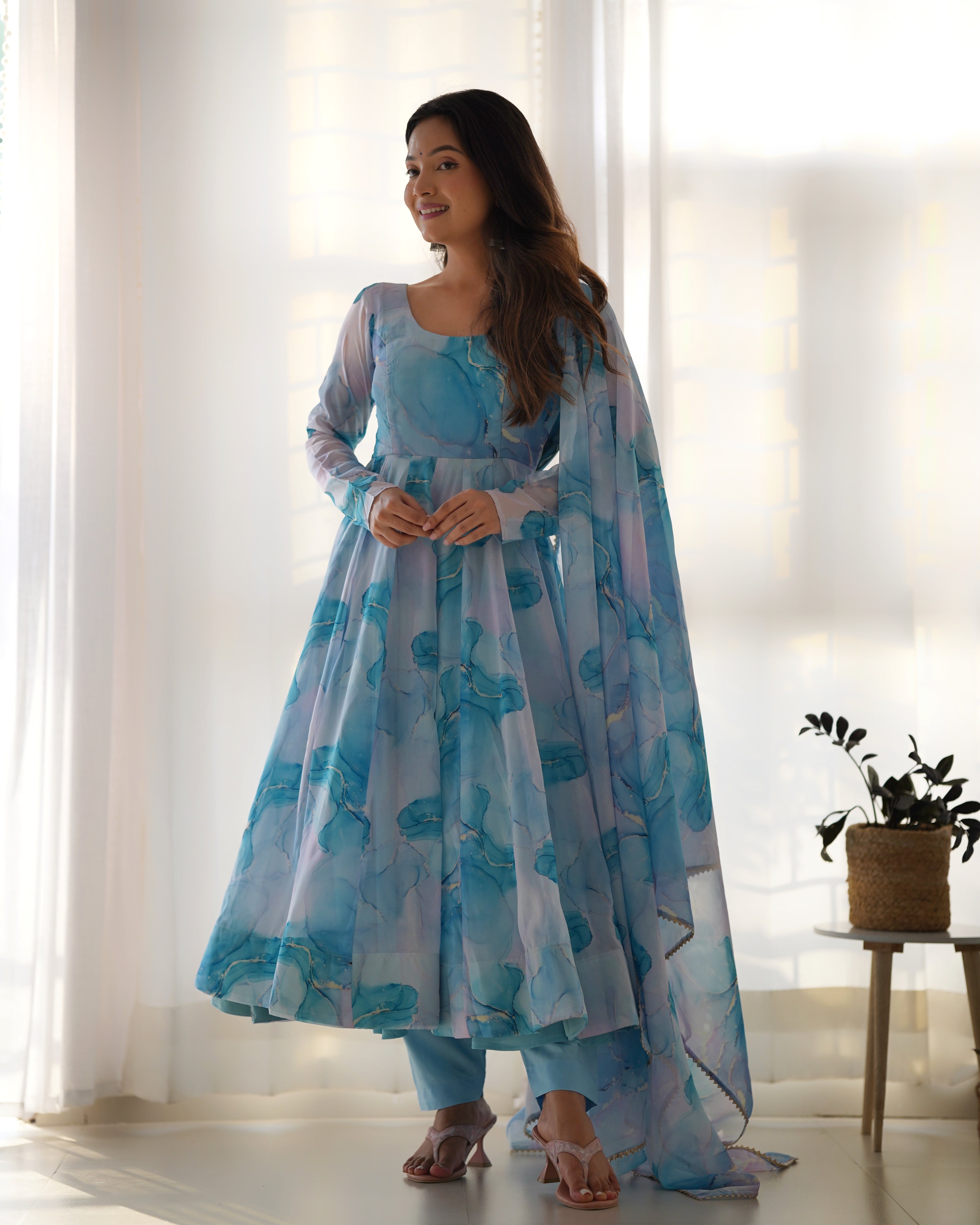 Woman wearing a light blue floral dress with a sheer dupatta in a bright room.