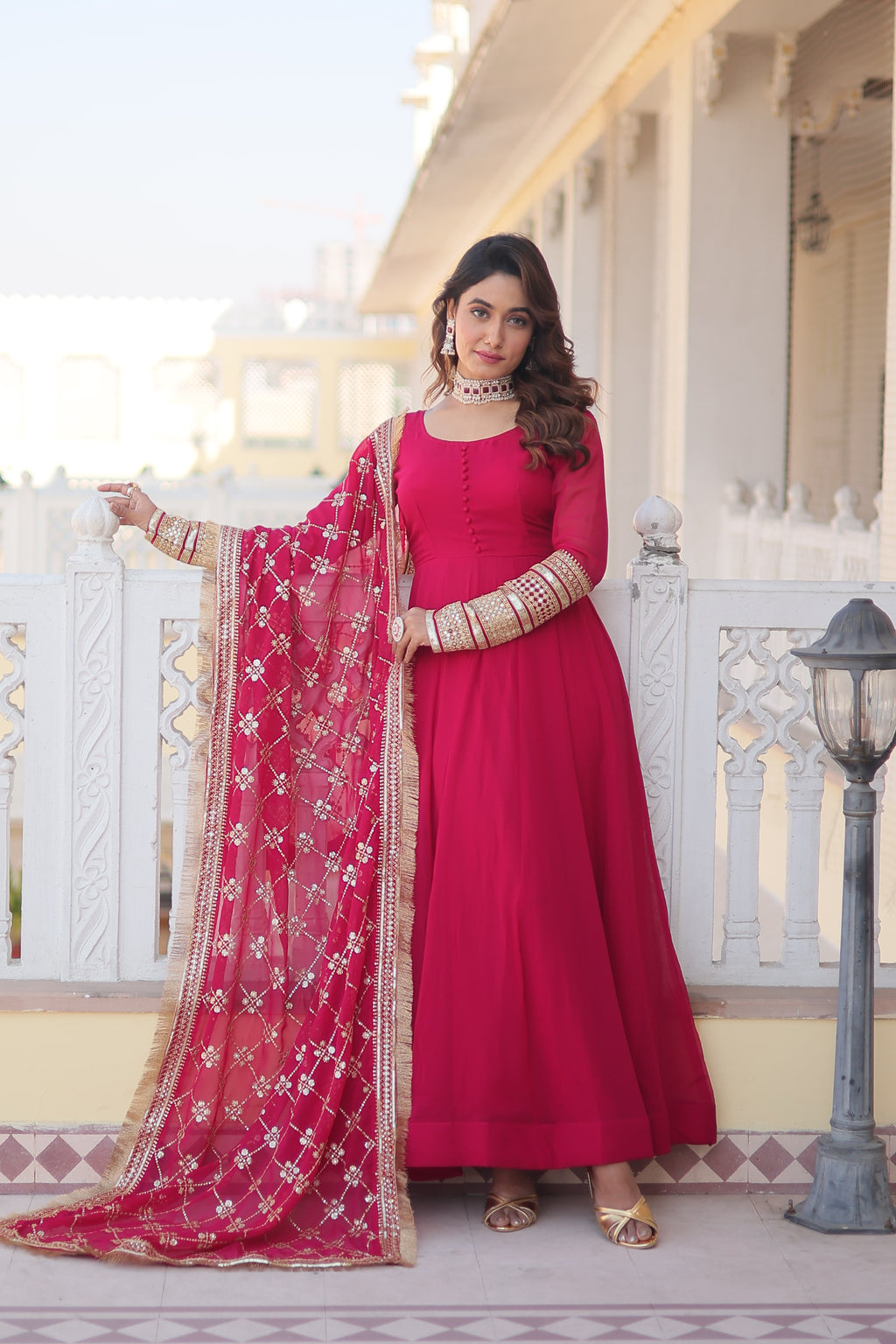 Woman in a pink traditional outfit with a red dupatta standing on a staircase.