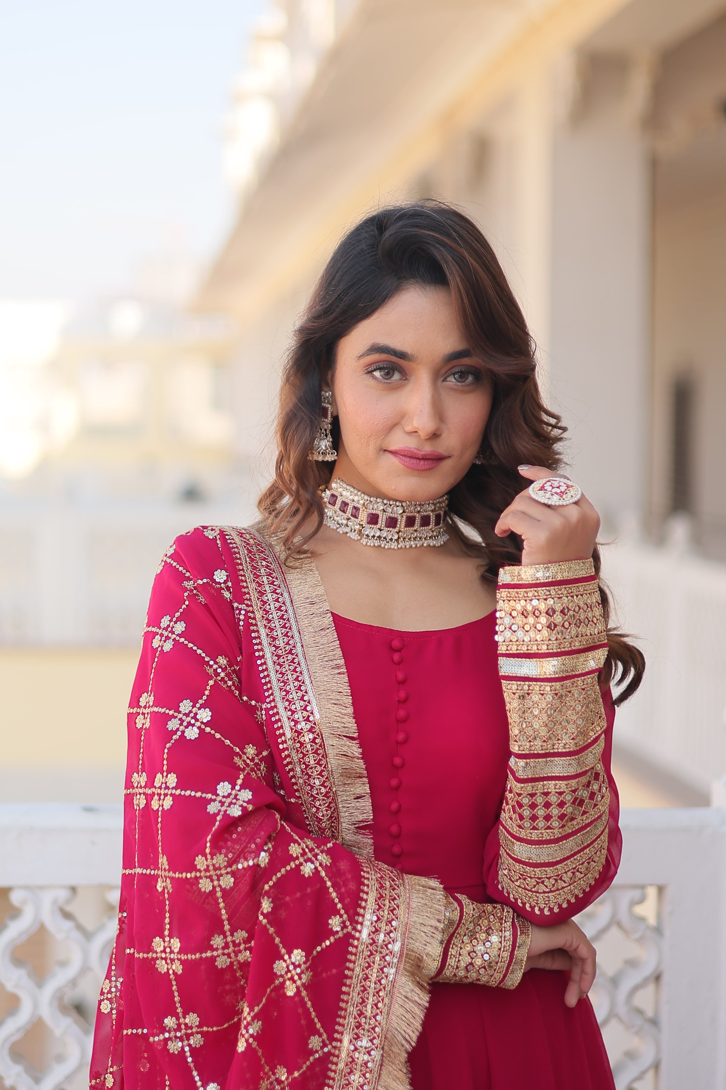 Woman in a red and gold traditional outfit with jewelry indoors.