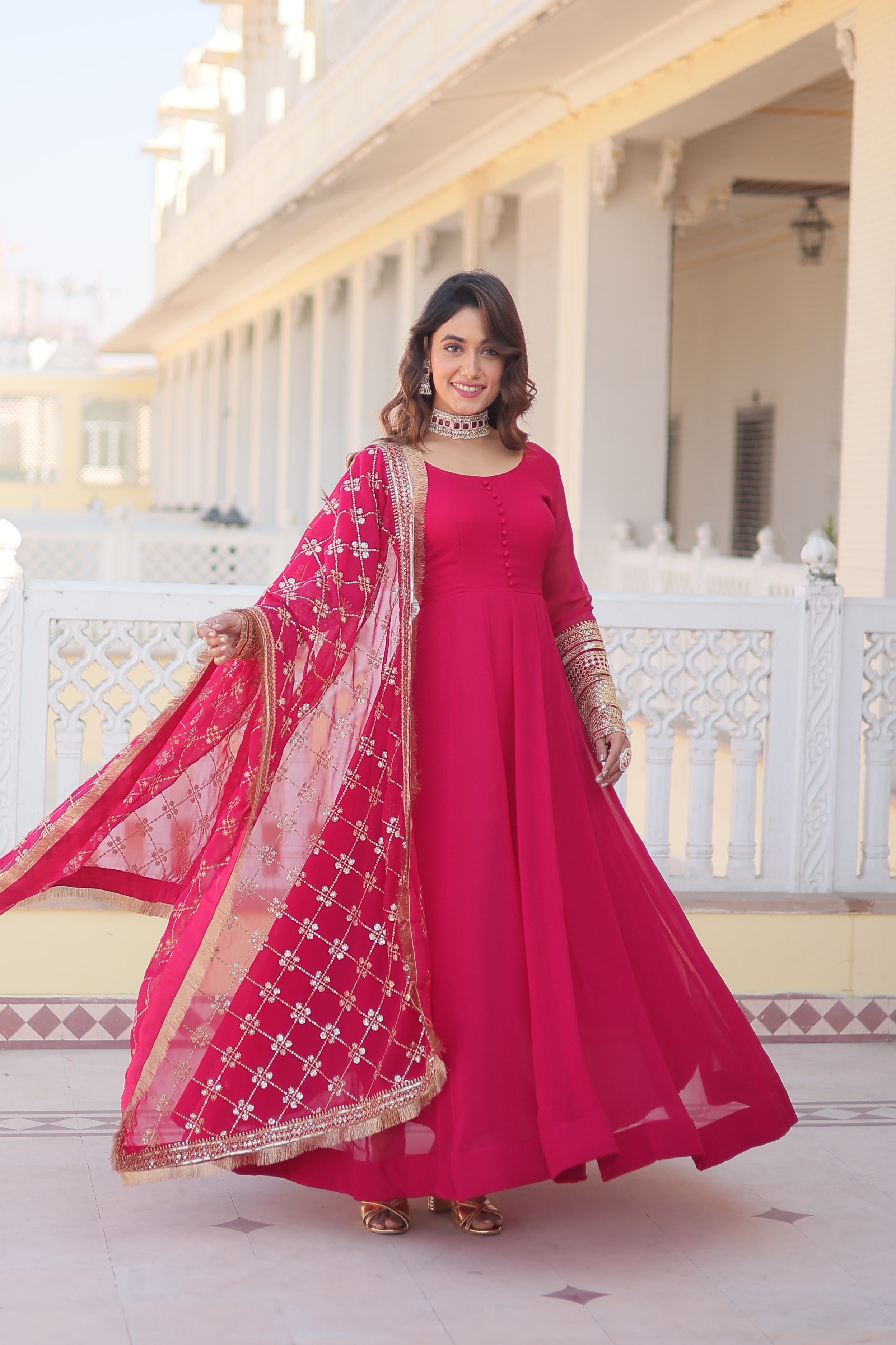 Woman in a bright pink traditional outfit with a matching dupatta standing in front of a white staircase.