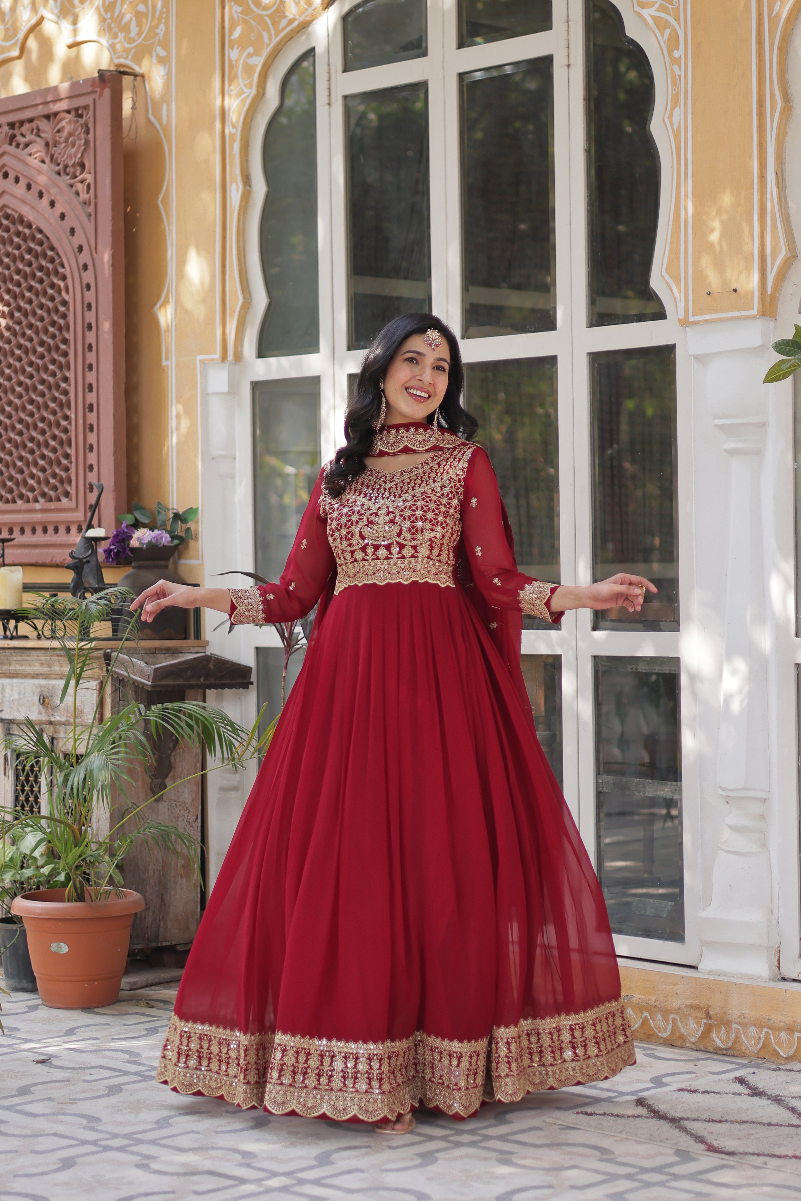 Woman in a red traditional outfit standing indoors with decorative elements.