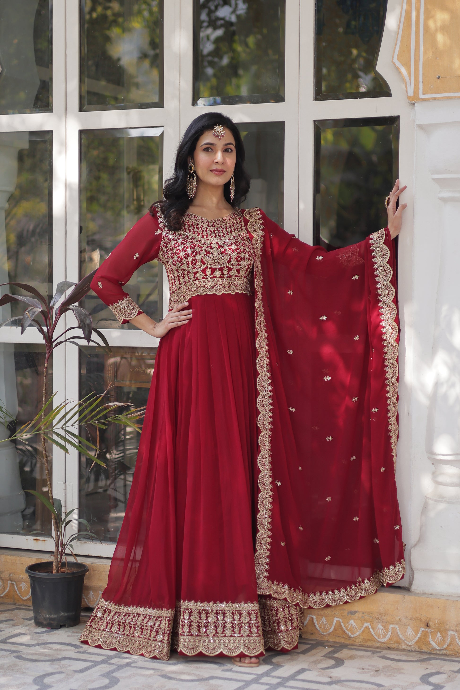 Woman wearing a red traditional outfit with gold embroidery indoors.