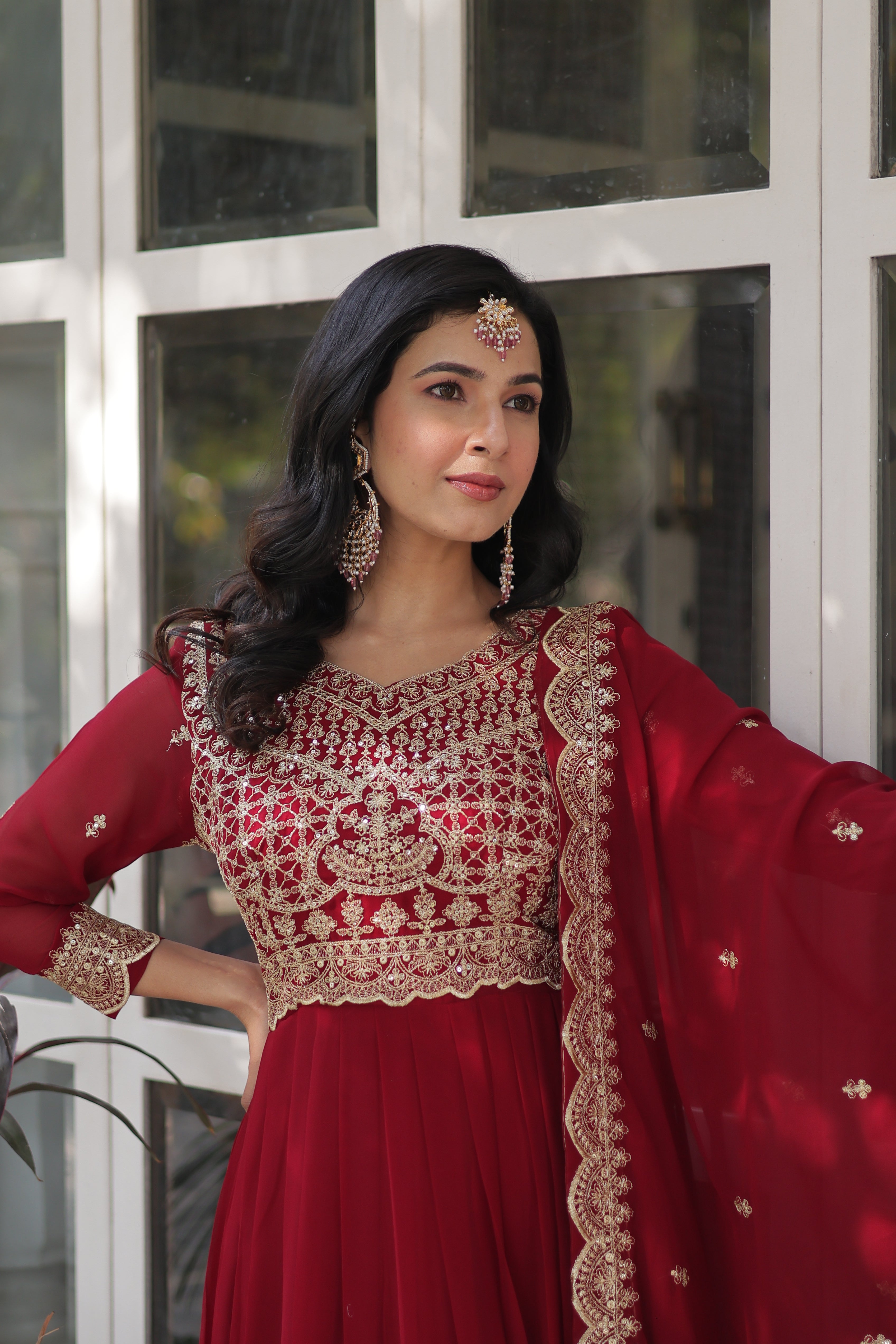 Woman in a red traditional outfit with gold embroidery standing indoors.