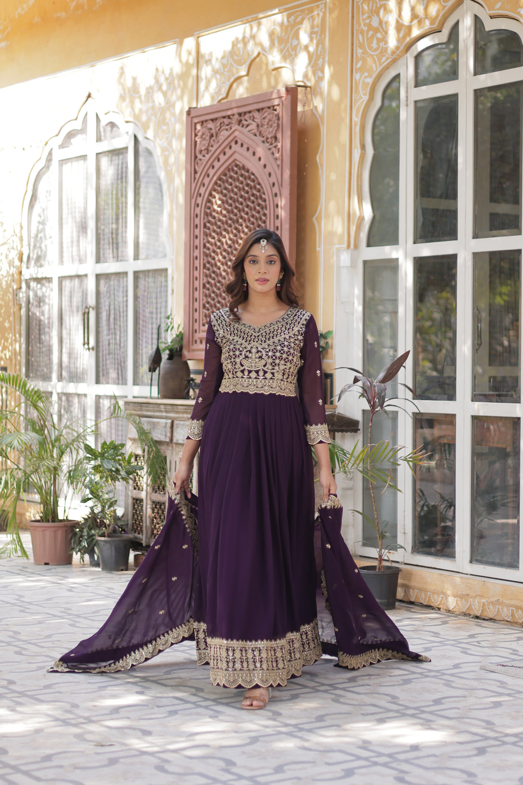 Woman in a purple dress standing in front of a decorative wall with geometric patterns.