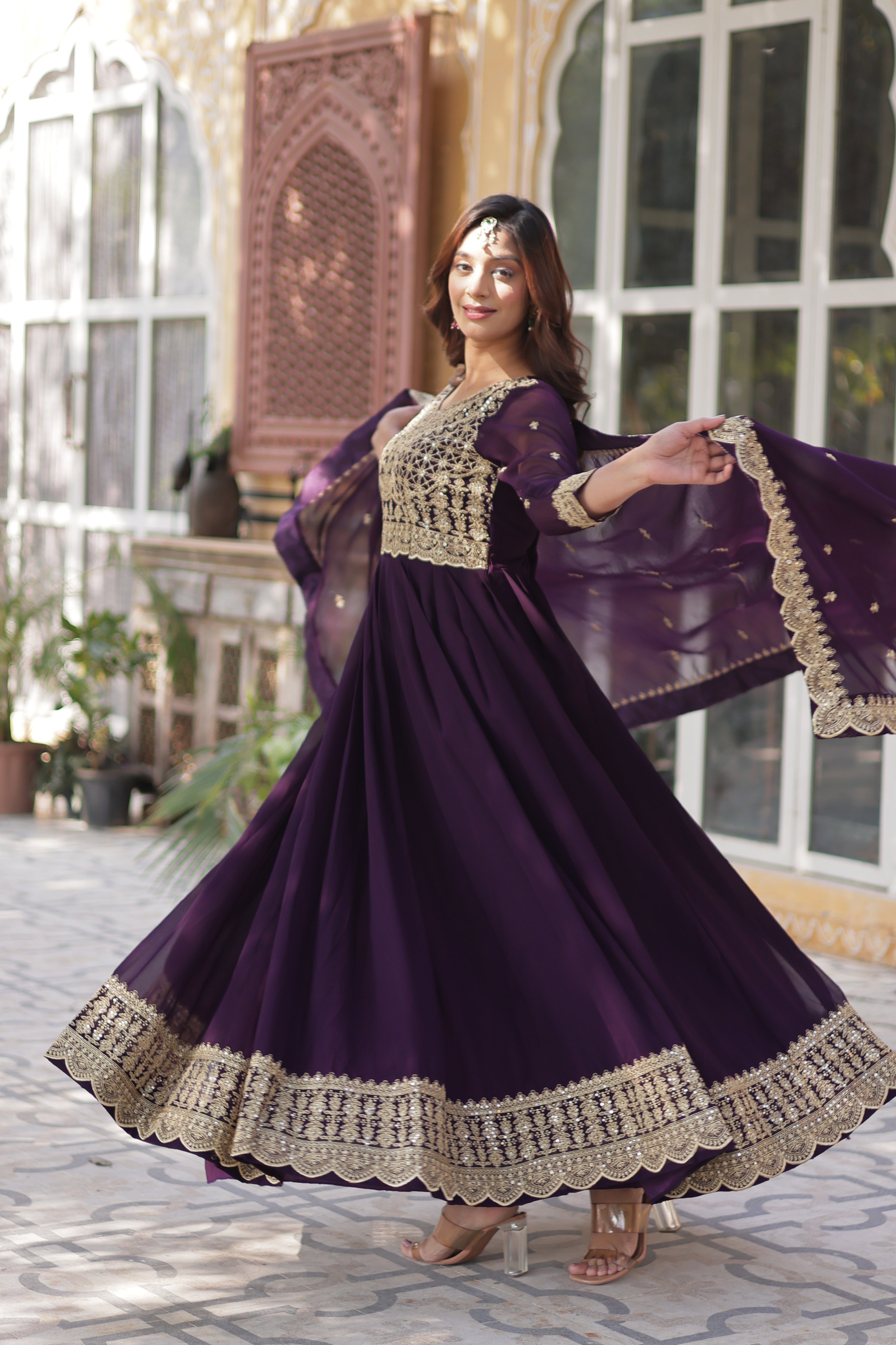 Woman in a purple dress with gold details posing outdoors.