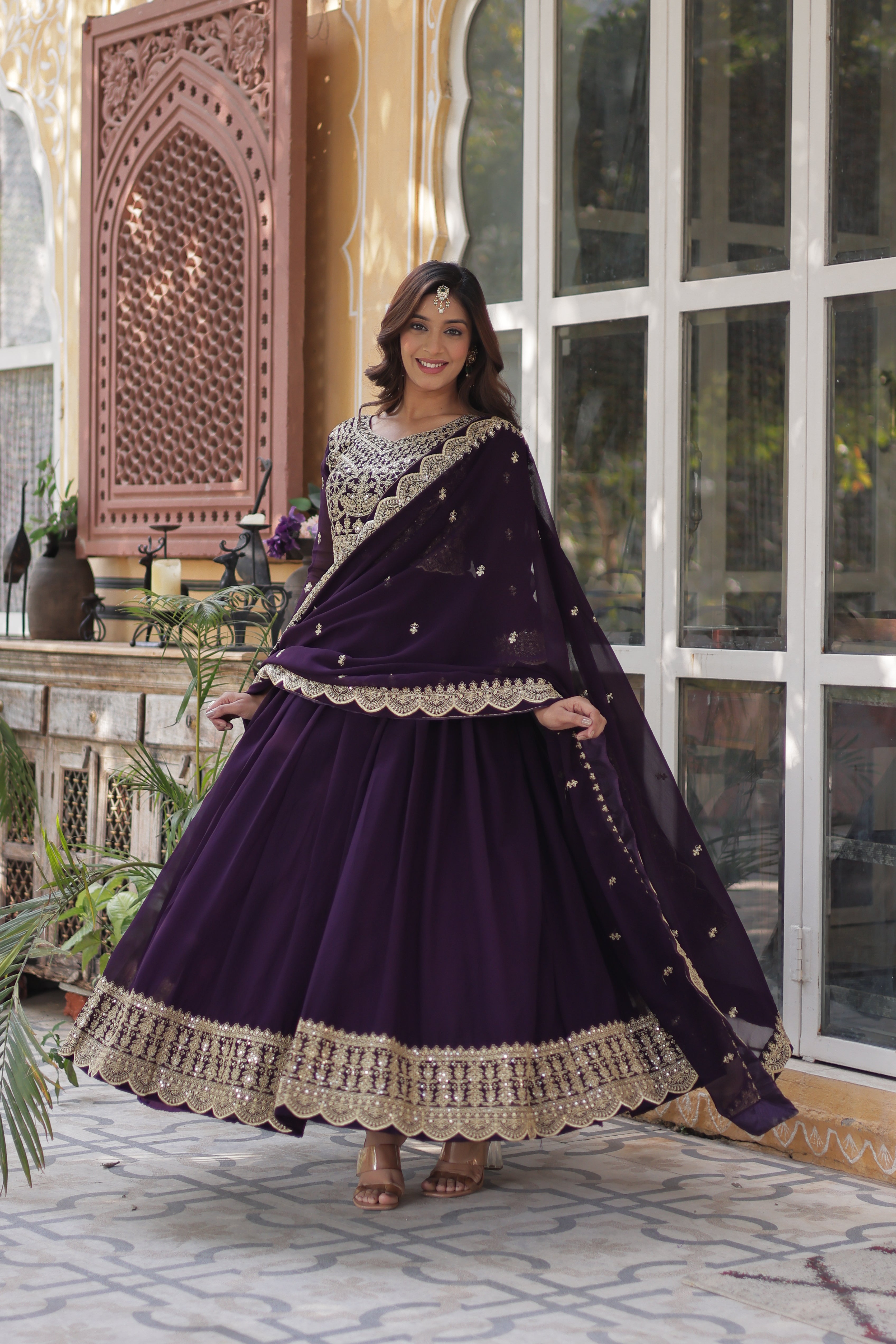 Woman in a purple dress with intricate detailing standing in front of a decorative door.