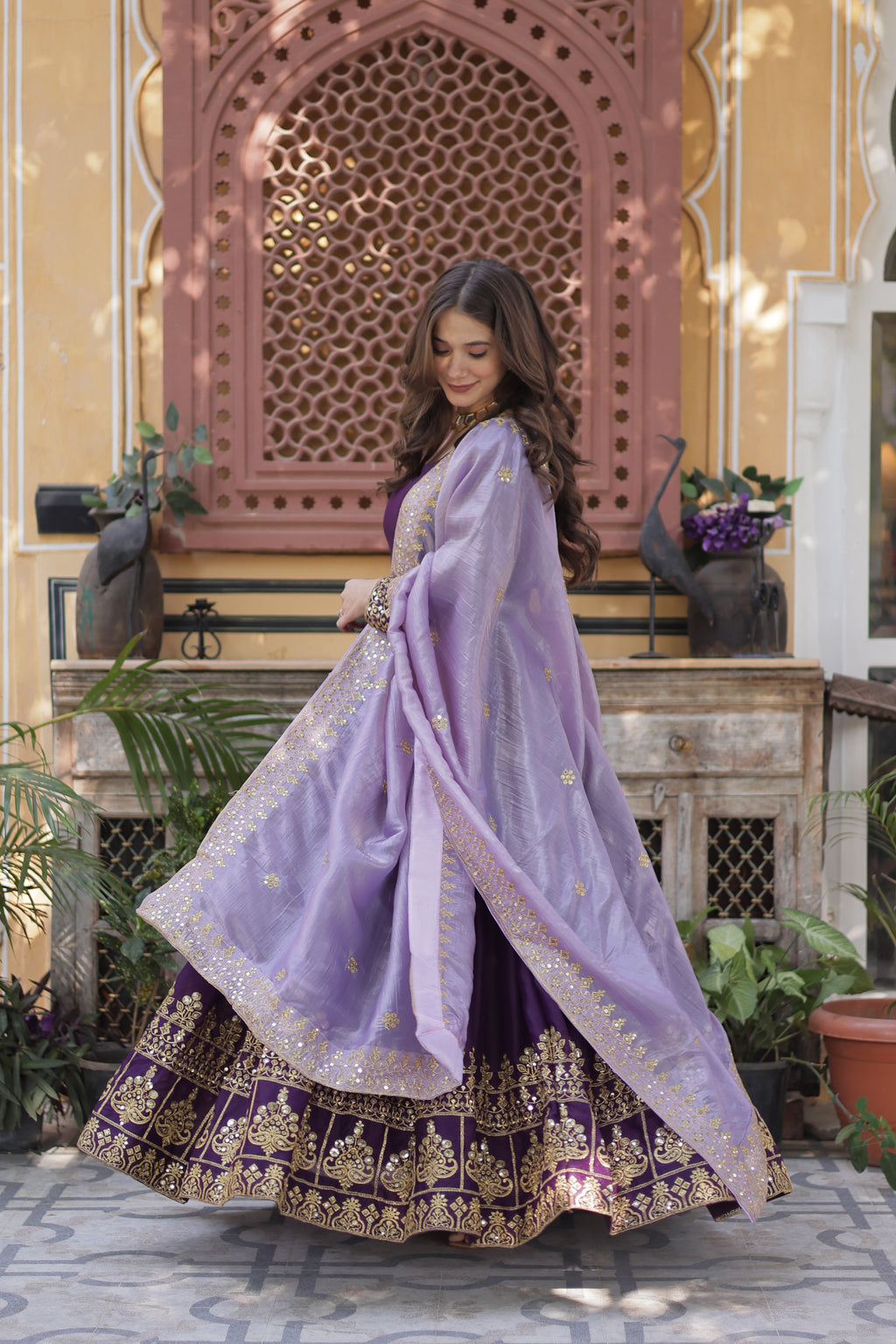 Woman in a traditional outfit with a purple shawl in front of a decorative building entrance.