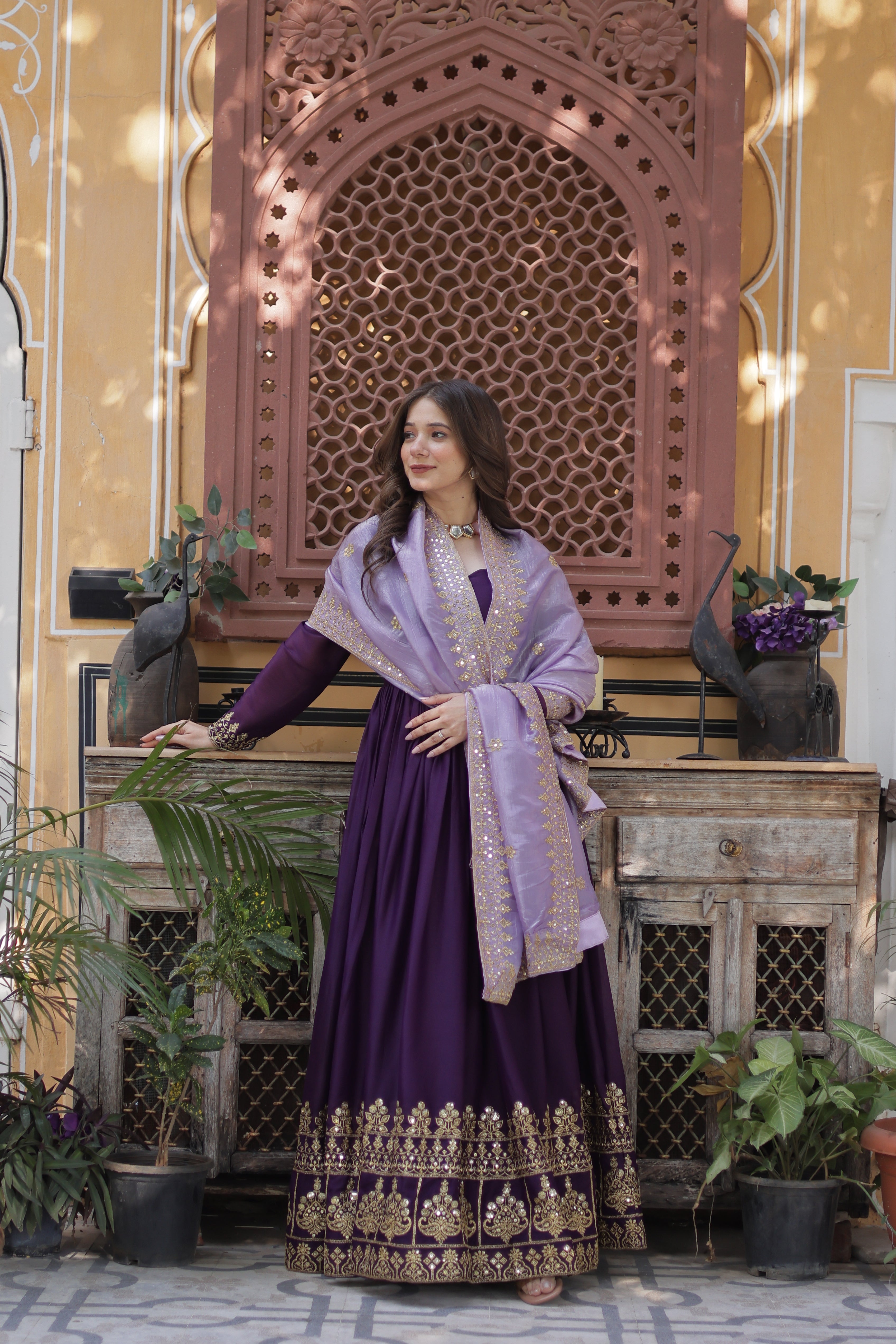 Woman in a purple dress standing in front of a decorative wall with plants.