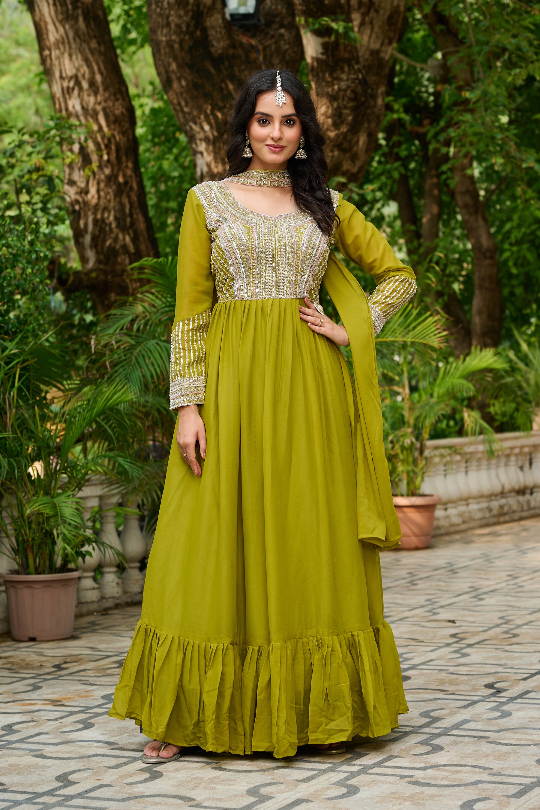 Woman in a green traditional outfit standing outdoors with trees in the background