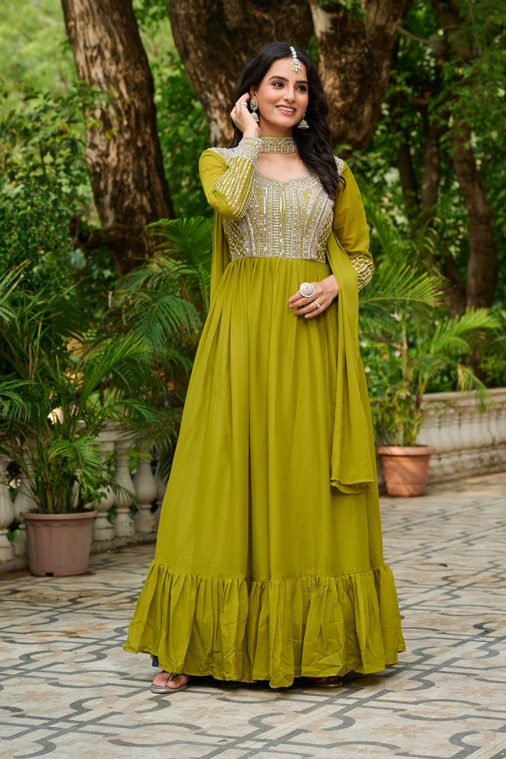 Woman in a green traditional outfit standing outdoors with greenery in the background