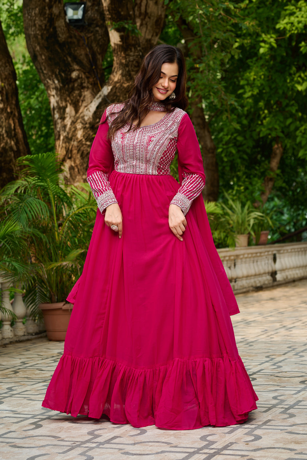 Woman wearing a pink traditional outfit with intricate patterns in an outdoor setting.