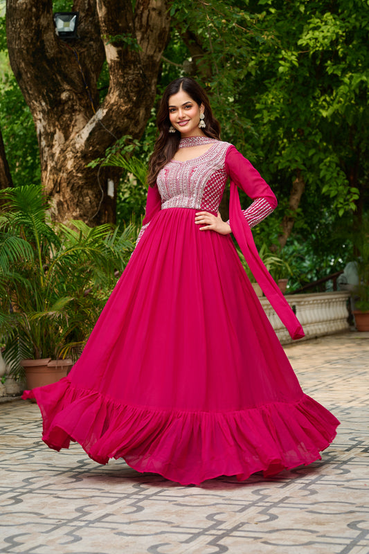 Woman in a pink traditional outfit standing outdoors with greenery in the background