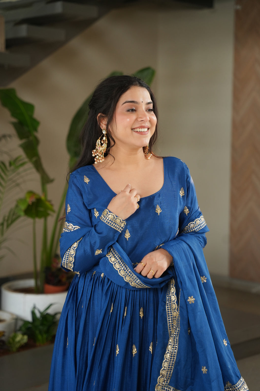 Woman in a blue traditional outfit with gold embroidery, smiling indoors.