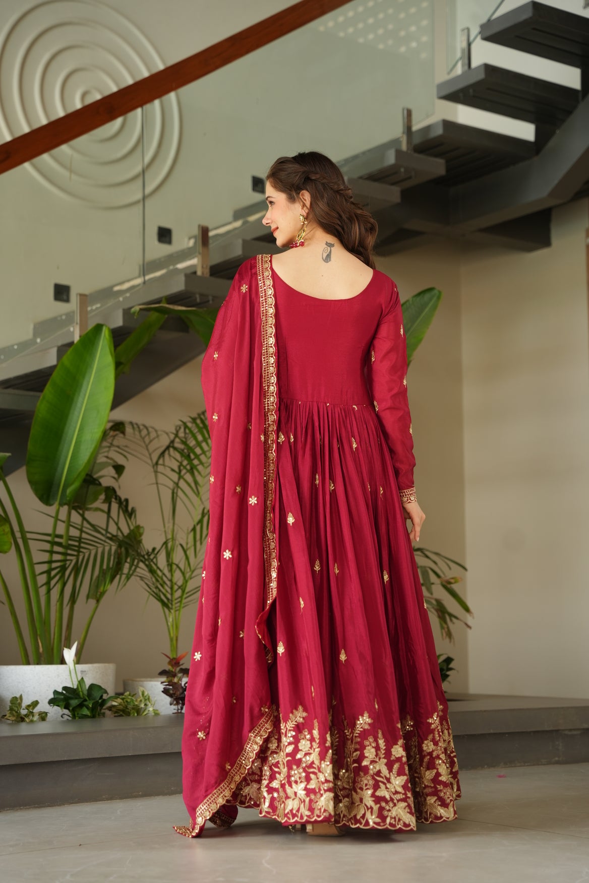 Woman in a red dress with gold details standing indoors with plants in the background