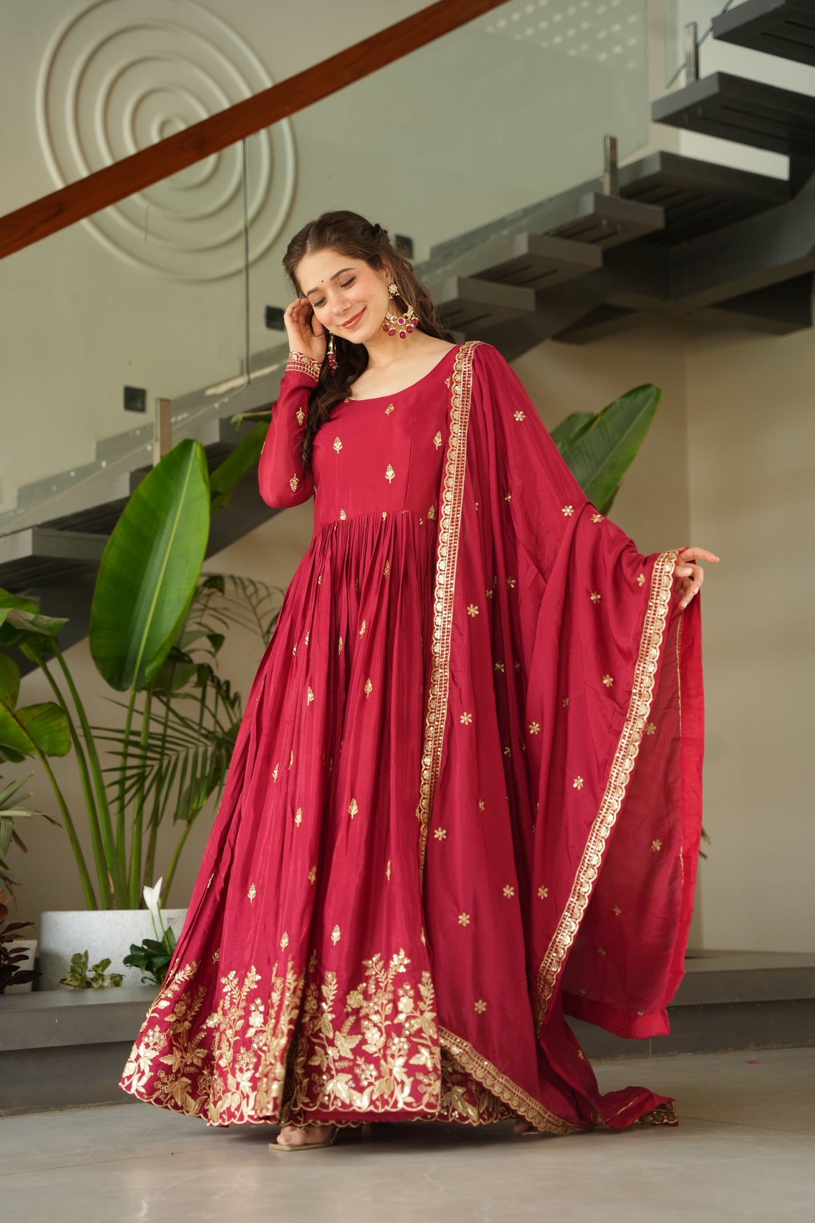 Woman in a red traditional outfit with gold details standing indoors.