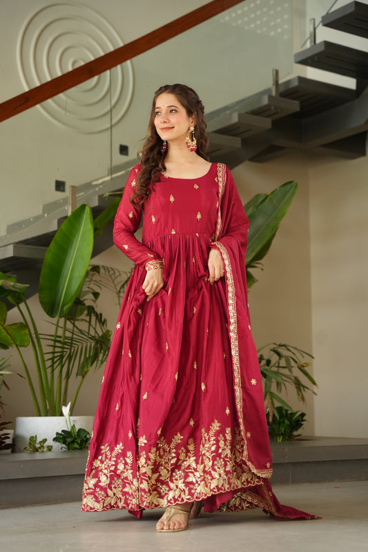 Woman in a red traditional outfit with gold patterns standing indoors.