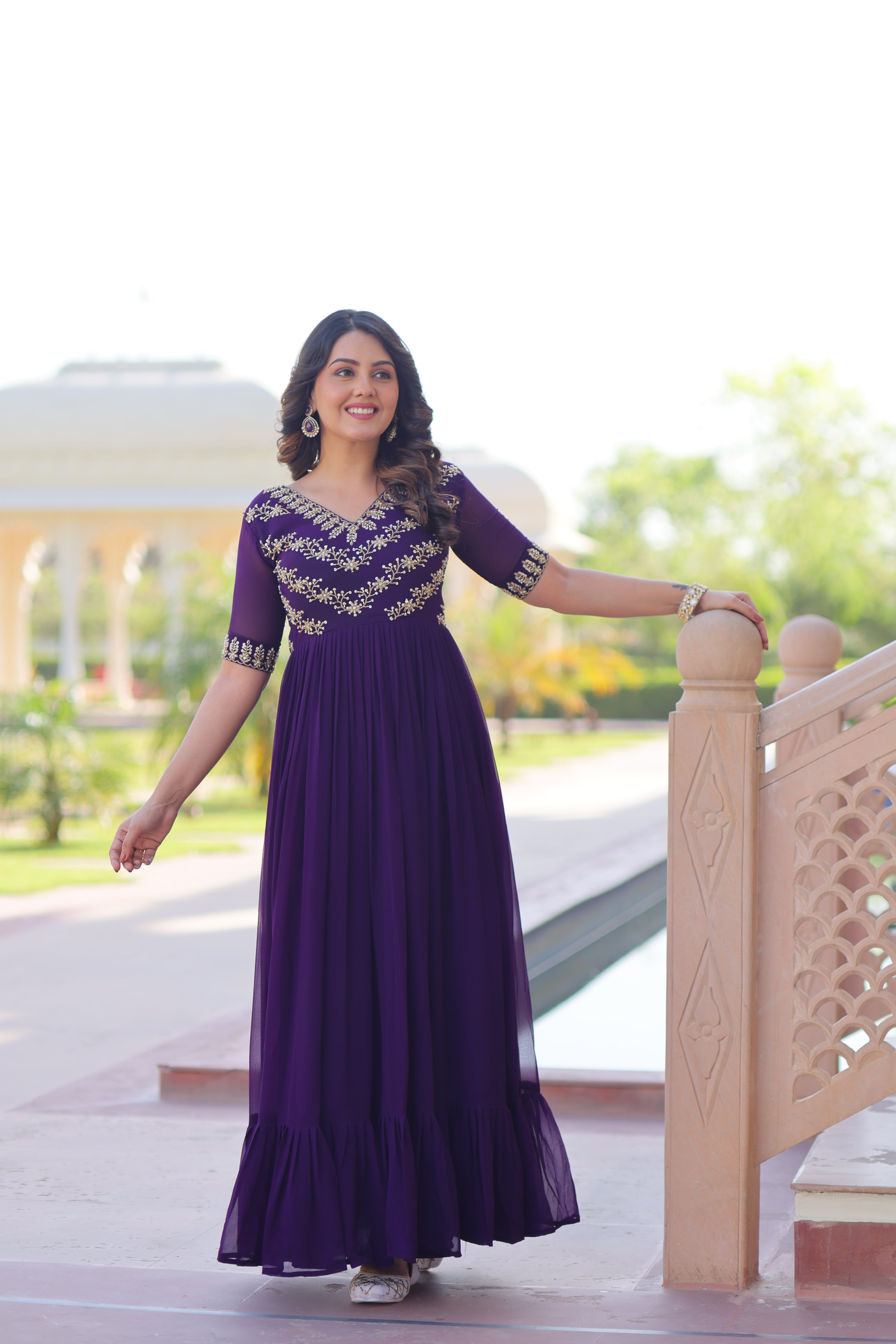 Woman in a purple dress with gold embroidery standing on a staircase.
