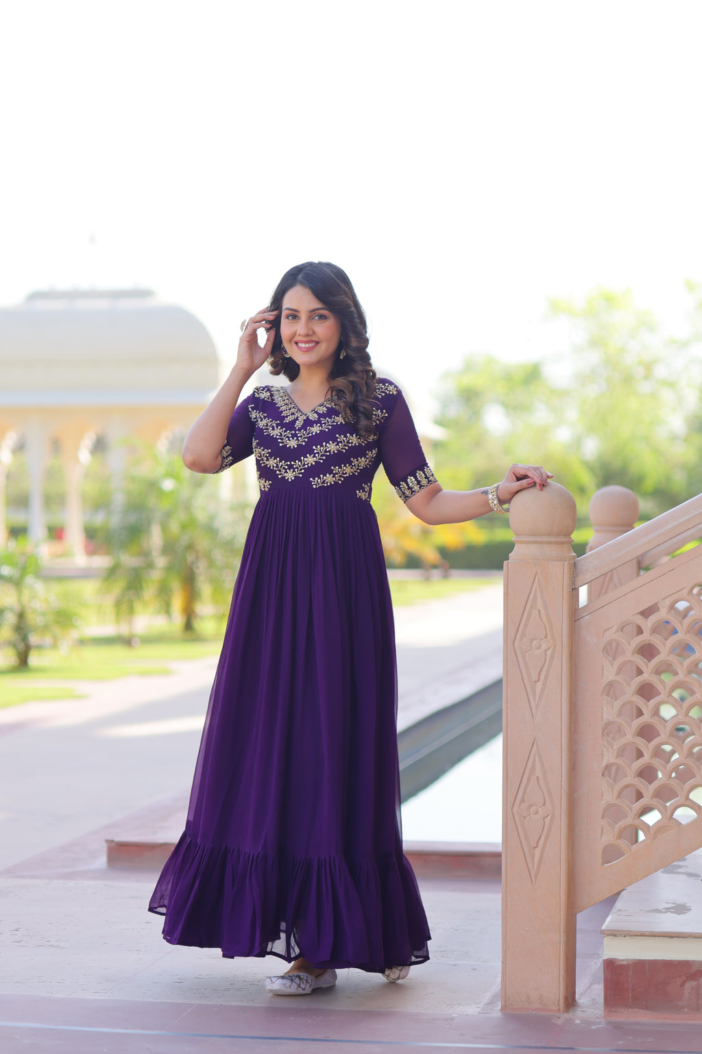 Woman in a purple dress standing on a staircase with greenery in the background