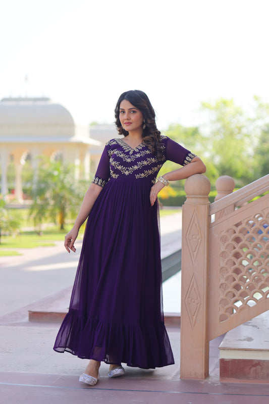 Woman in a purple dress standing on a wooden stool outdoors.