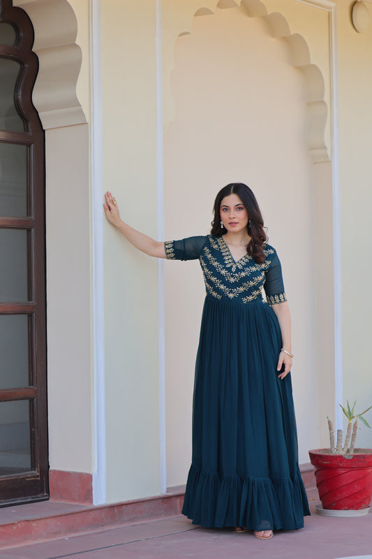 Woman in a blue evening gown standing against a plain wall.