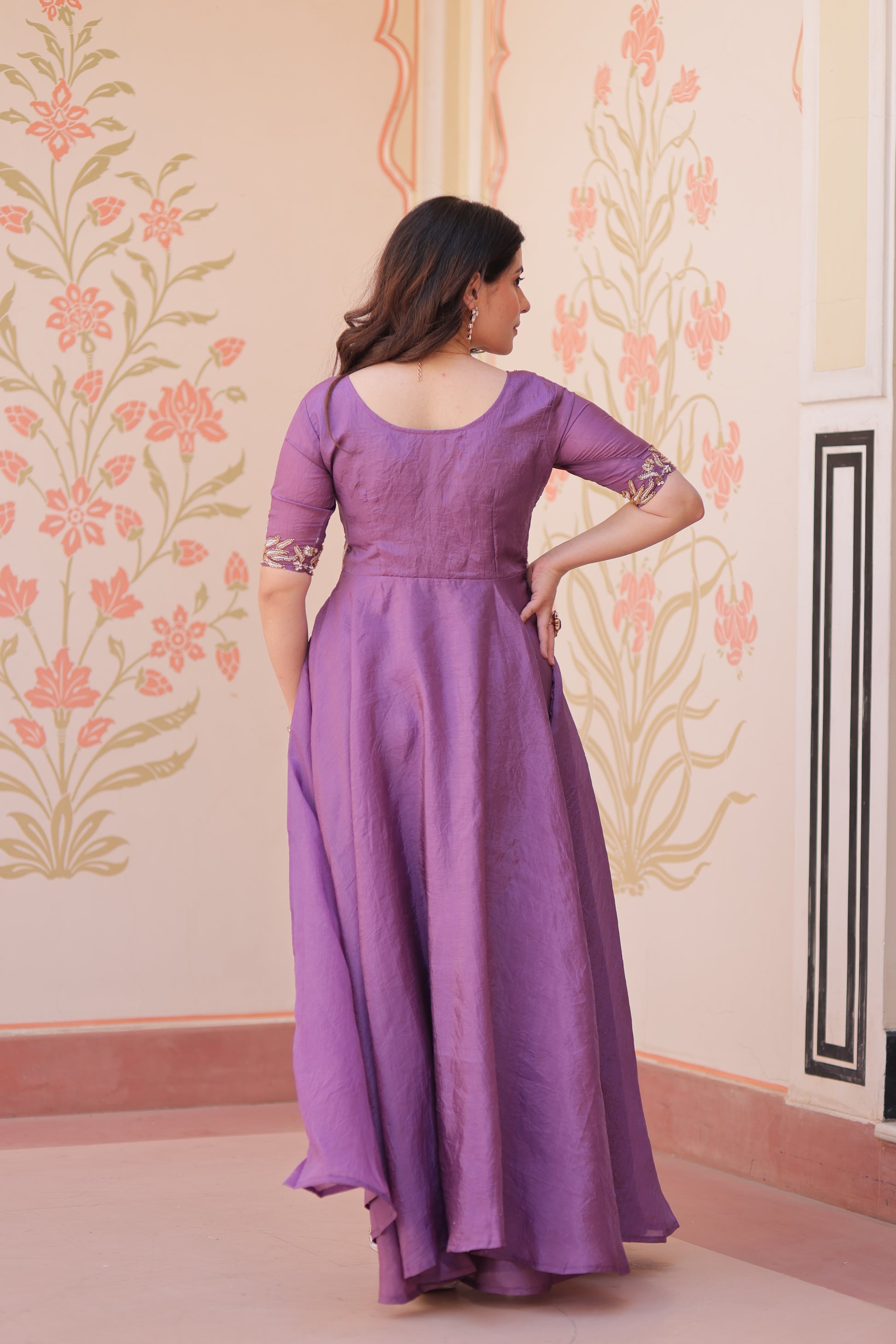Woman in a purple dress standing against a floral decorated wall.