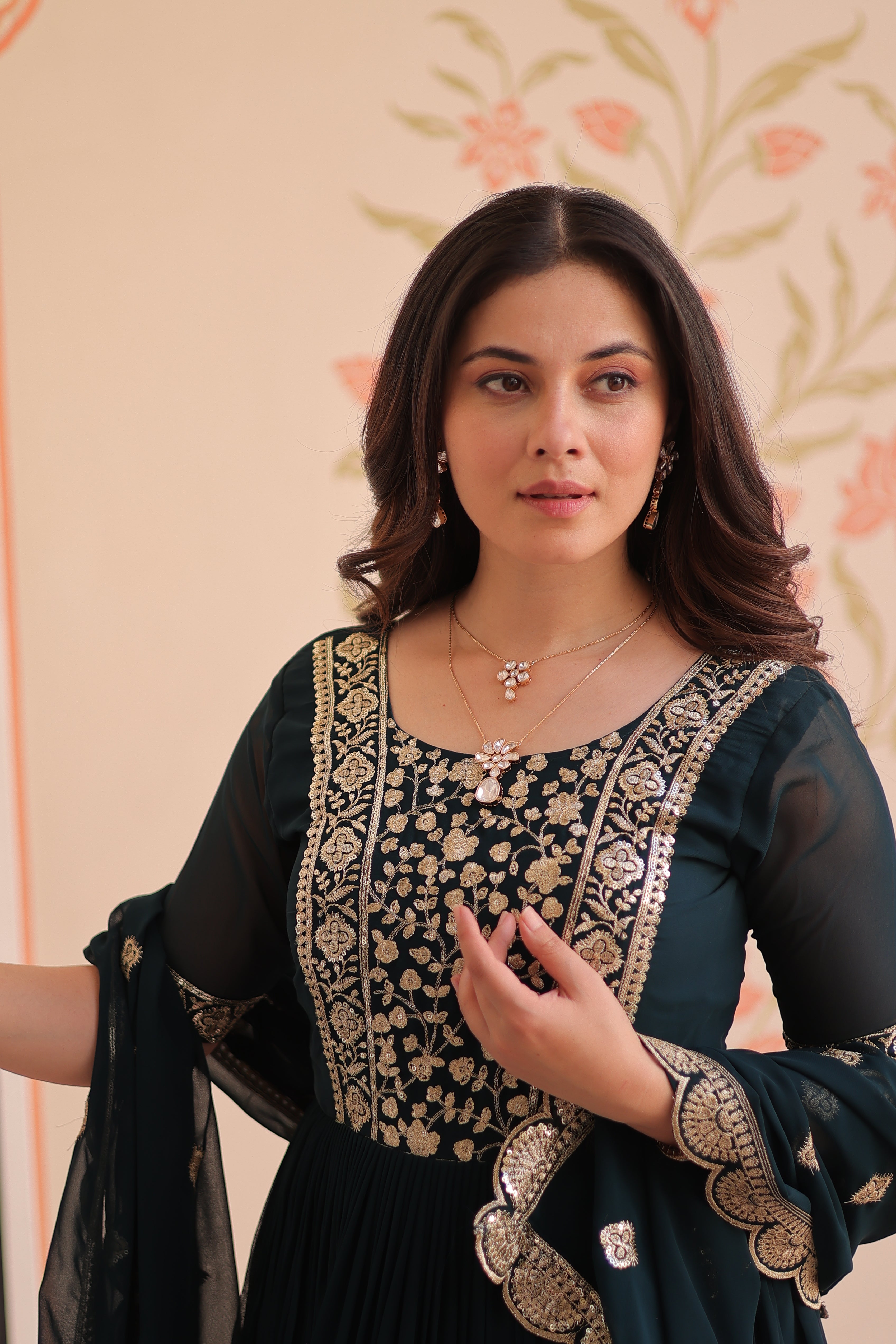 Woman wearing a dark blue traditional outfit with gold embroidery on a patterned background