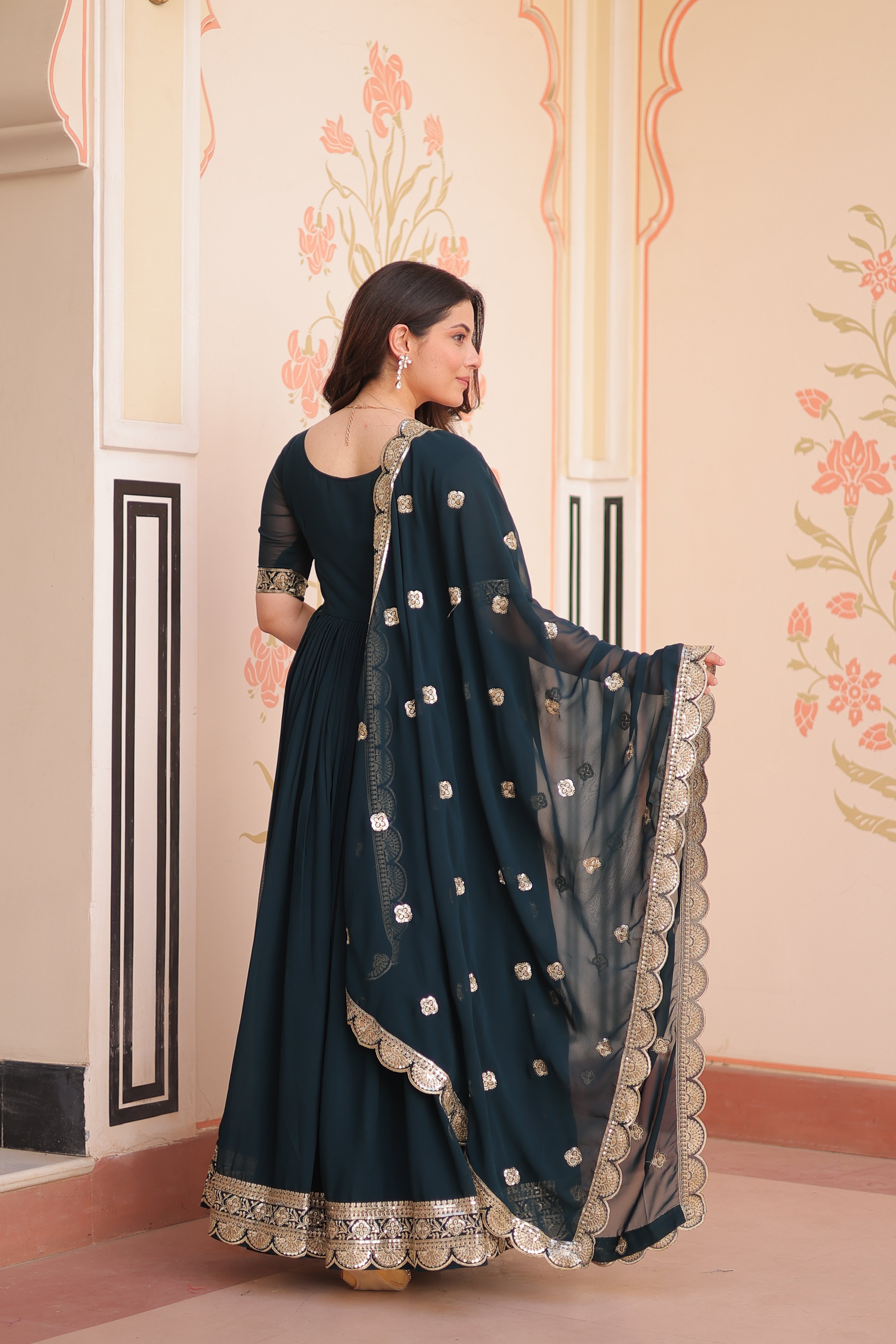 Woman wearing a dark blue traditional outfit with silver details in a decorative interior setting.