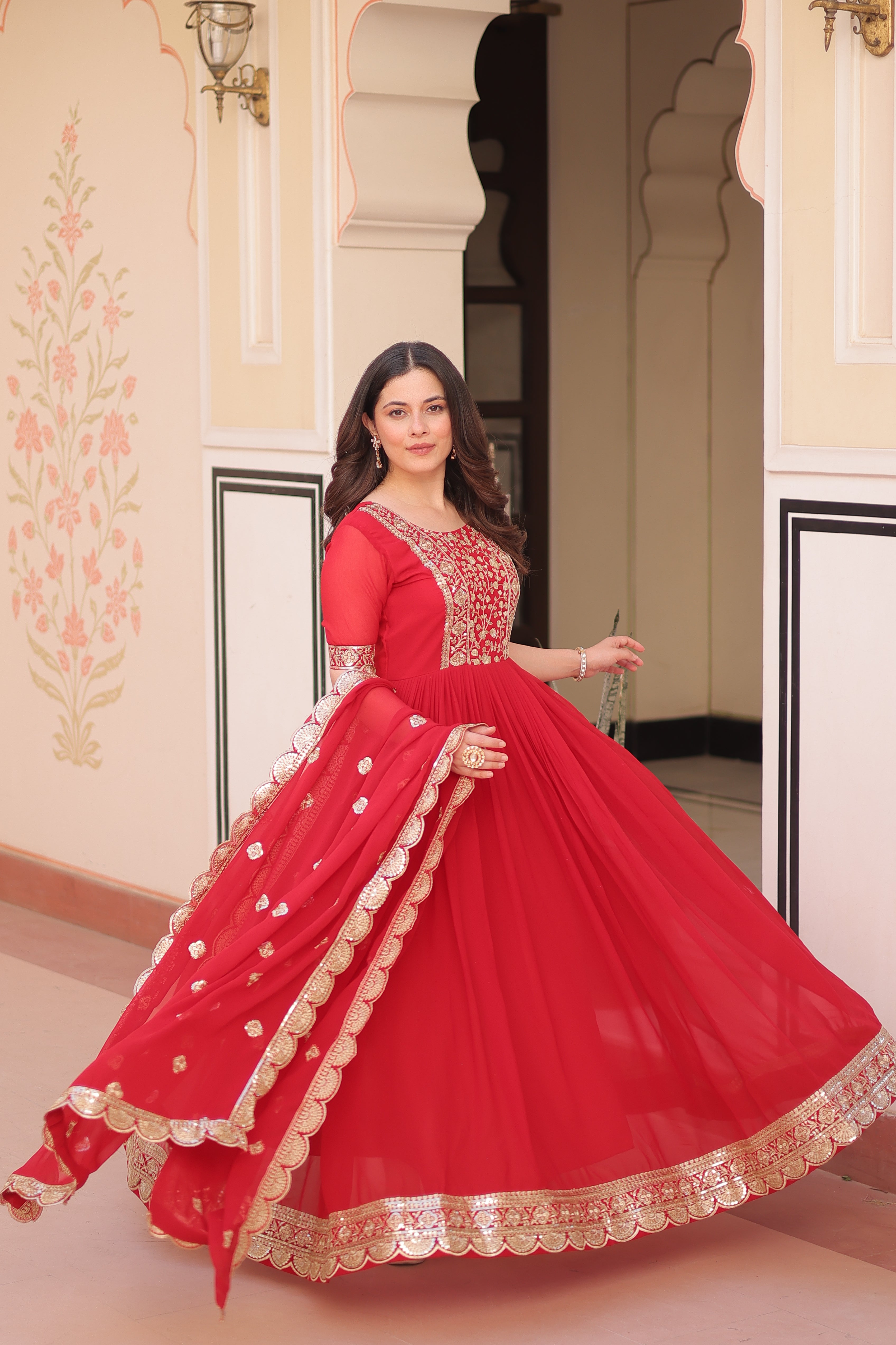 Woman in a red traditional outfit with gold embroidery standing in front of a mirror.