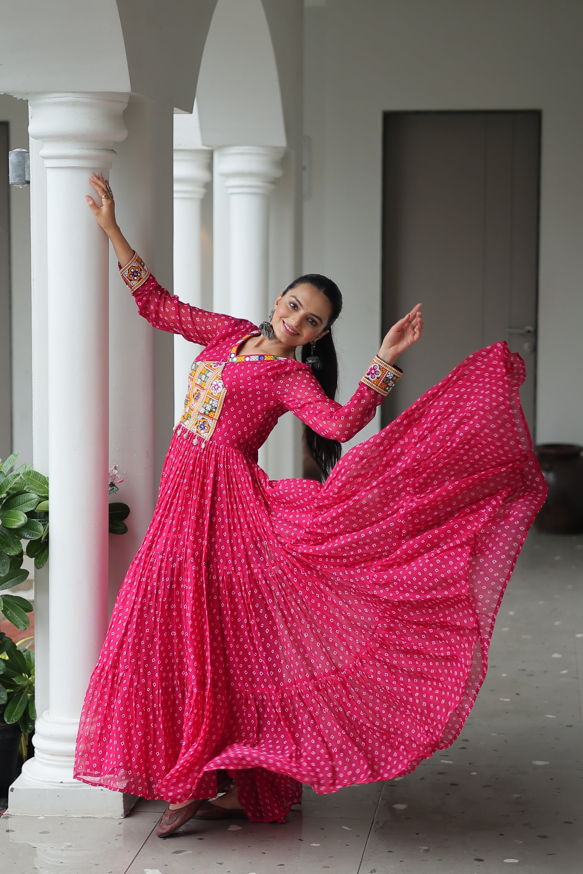 Woman in a bright pink traditional outfit with a long skirt, standing indoors.