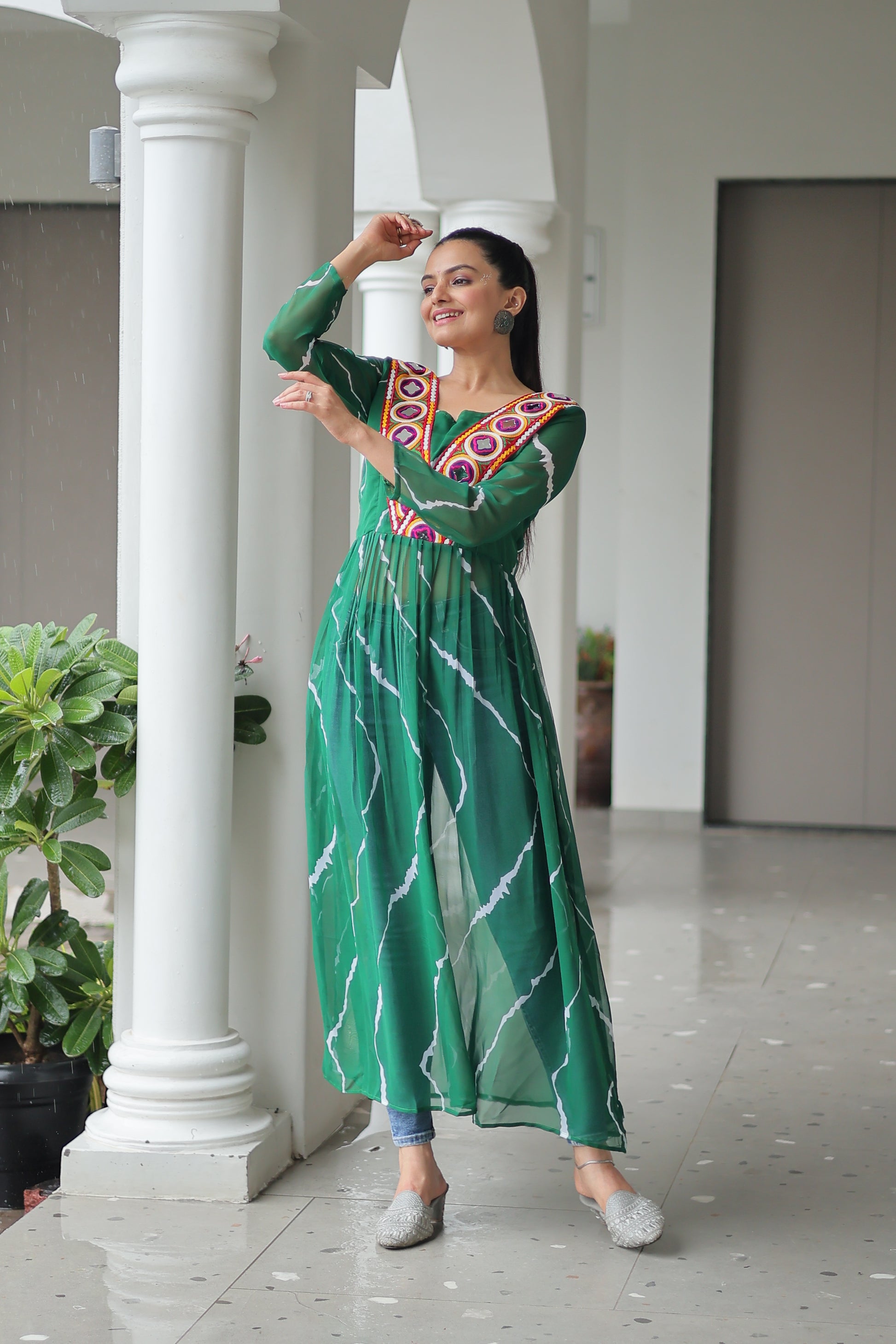 Woman in a green traditional outfit standing in front of white columns.