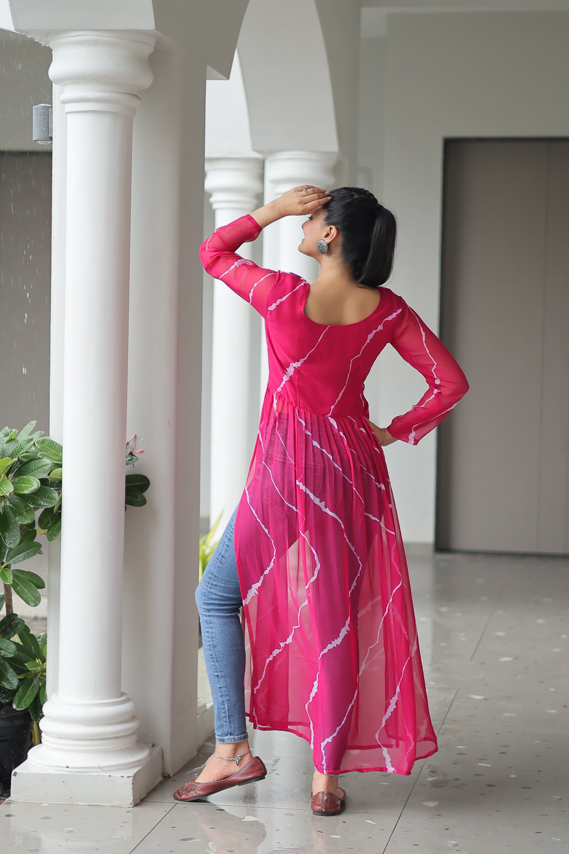 Woman in a pink dress standing between white columns with greenery above.