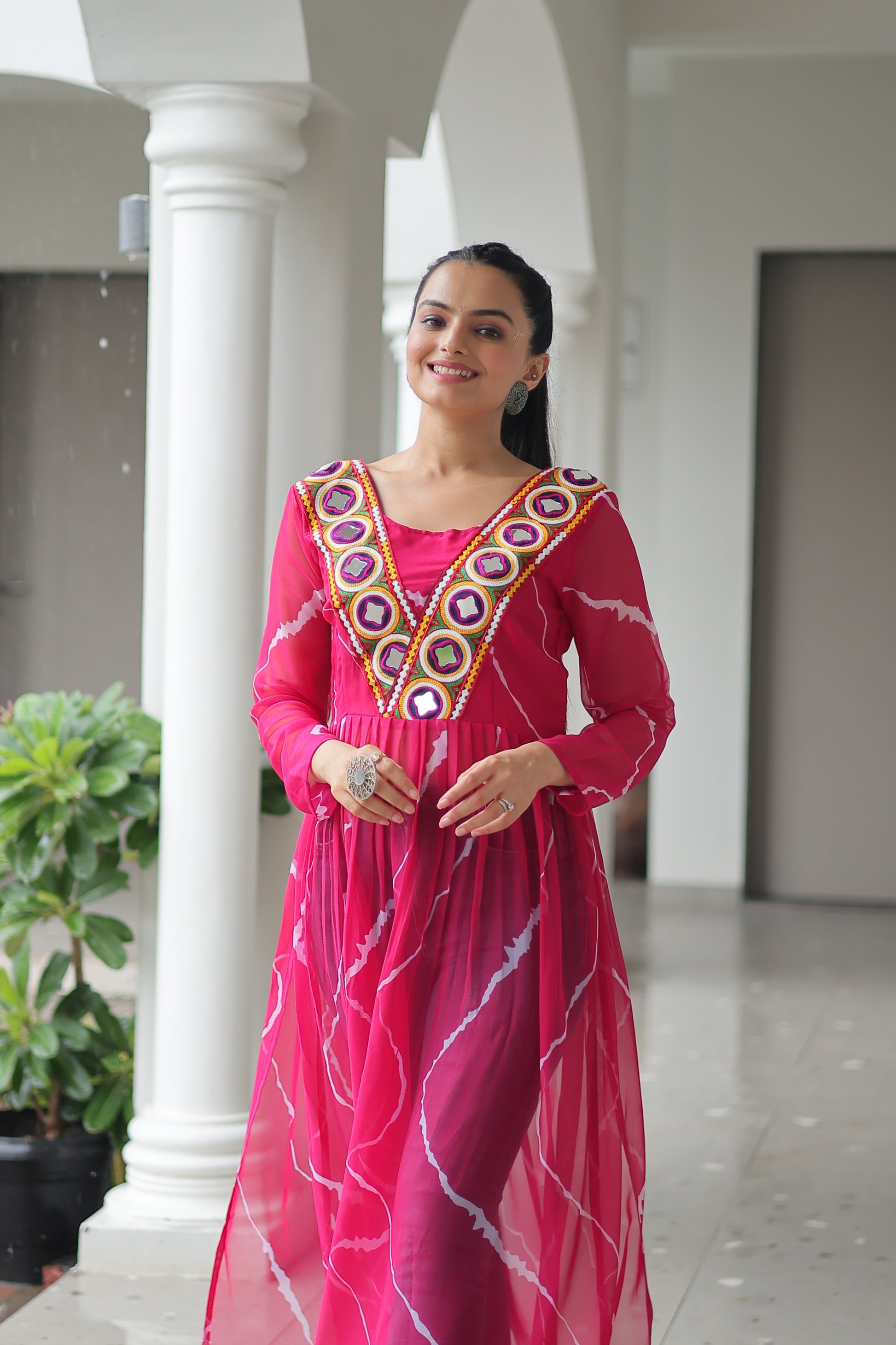 Woman in a pink traditional outfit with intricate patterns standing indoors.