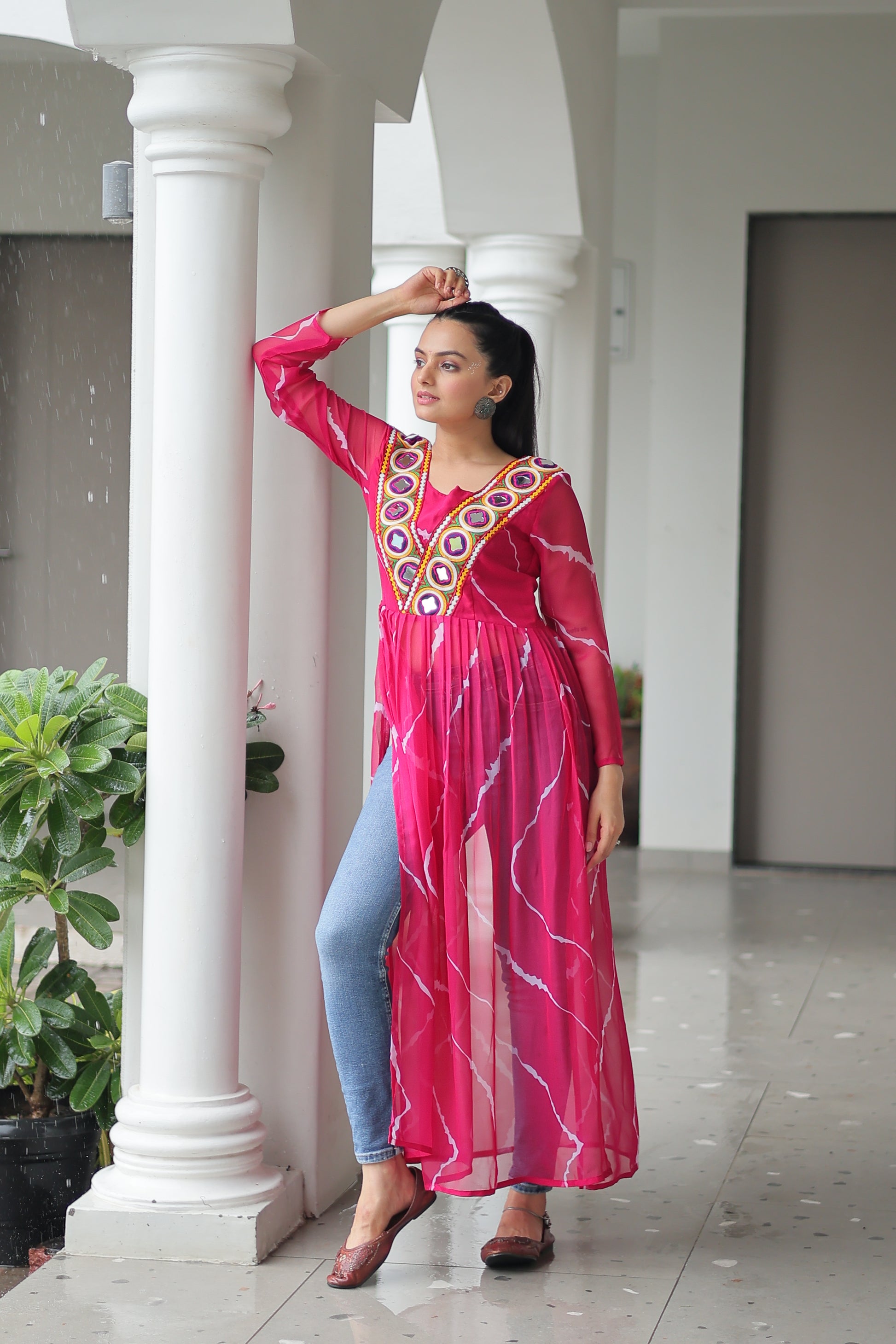 Woman in a pink traditional outfit standing in a well-lit indoor setting with white columns.