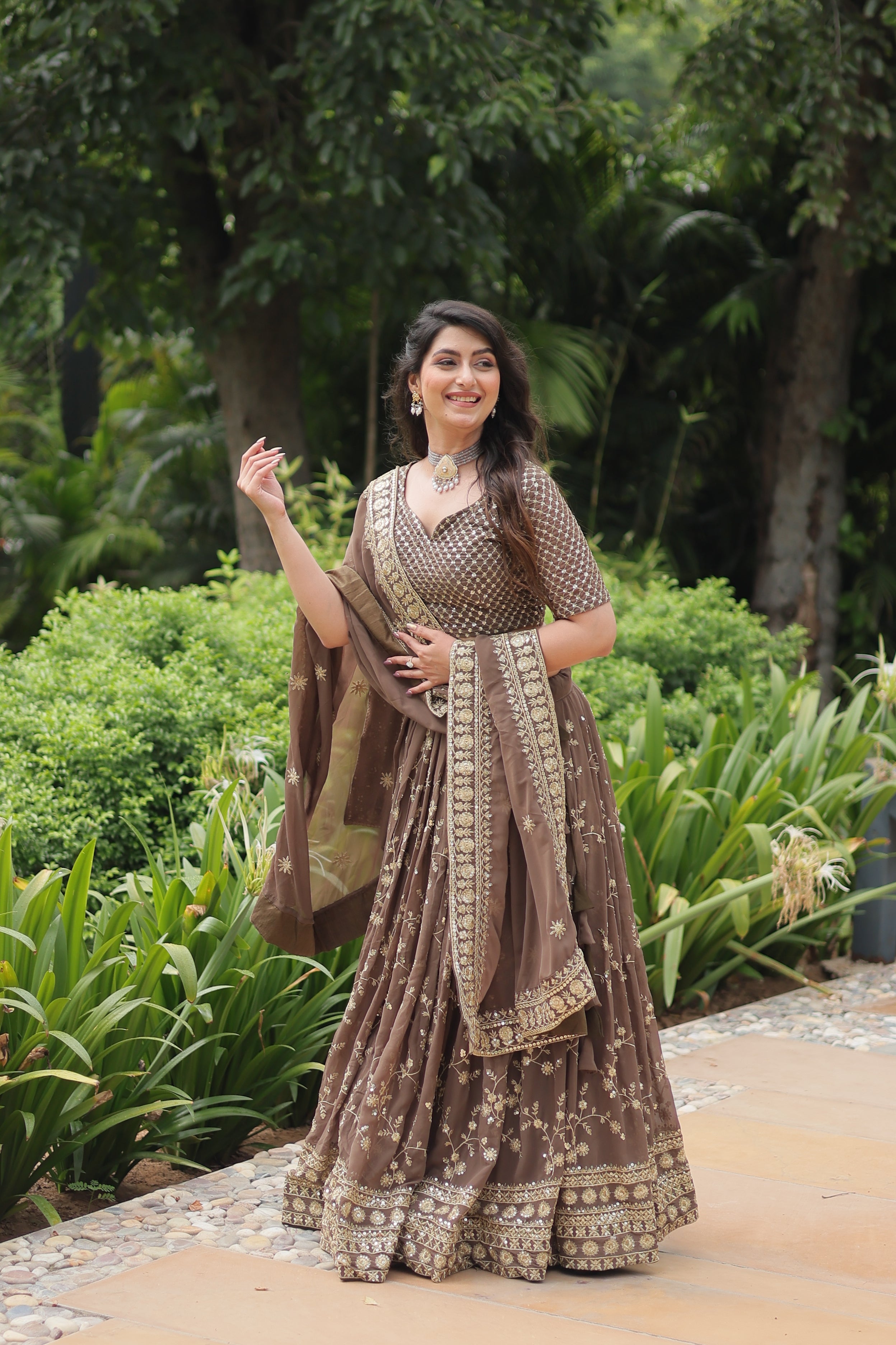 Woman in a traditional outfit standing outdoors with greenery in the background