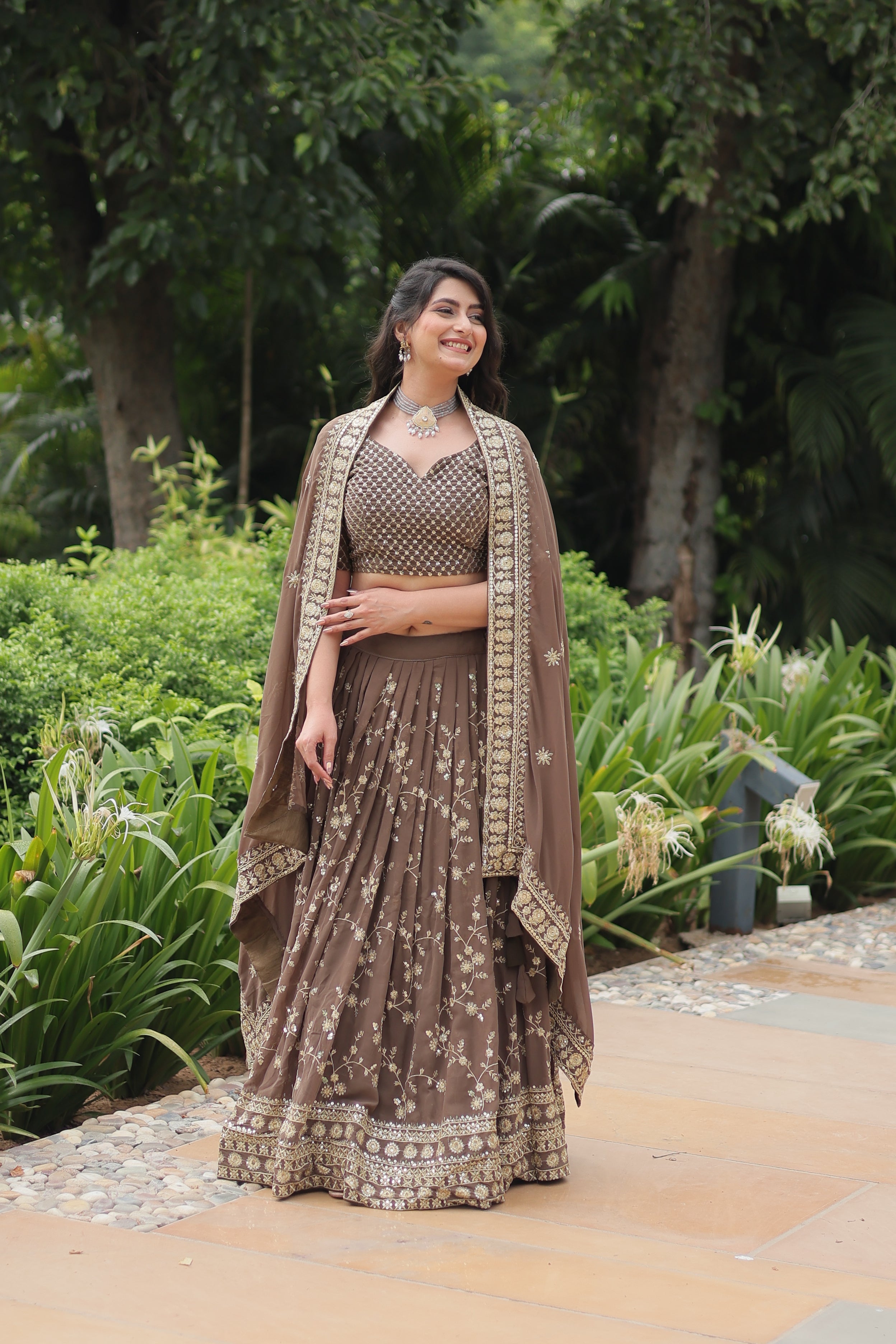 Woman in a traditional outfit standing outdoors with greenery in the background
