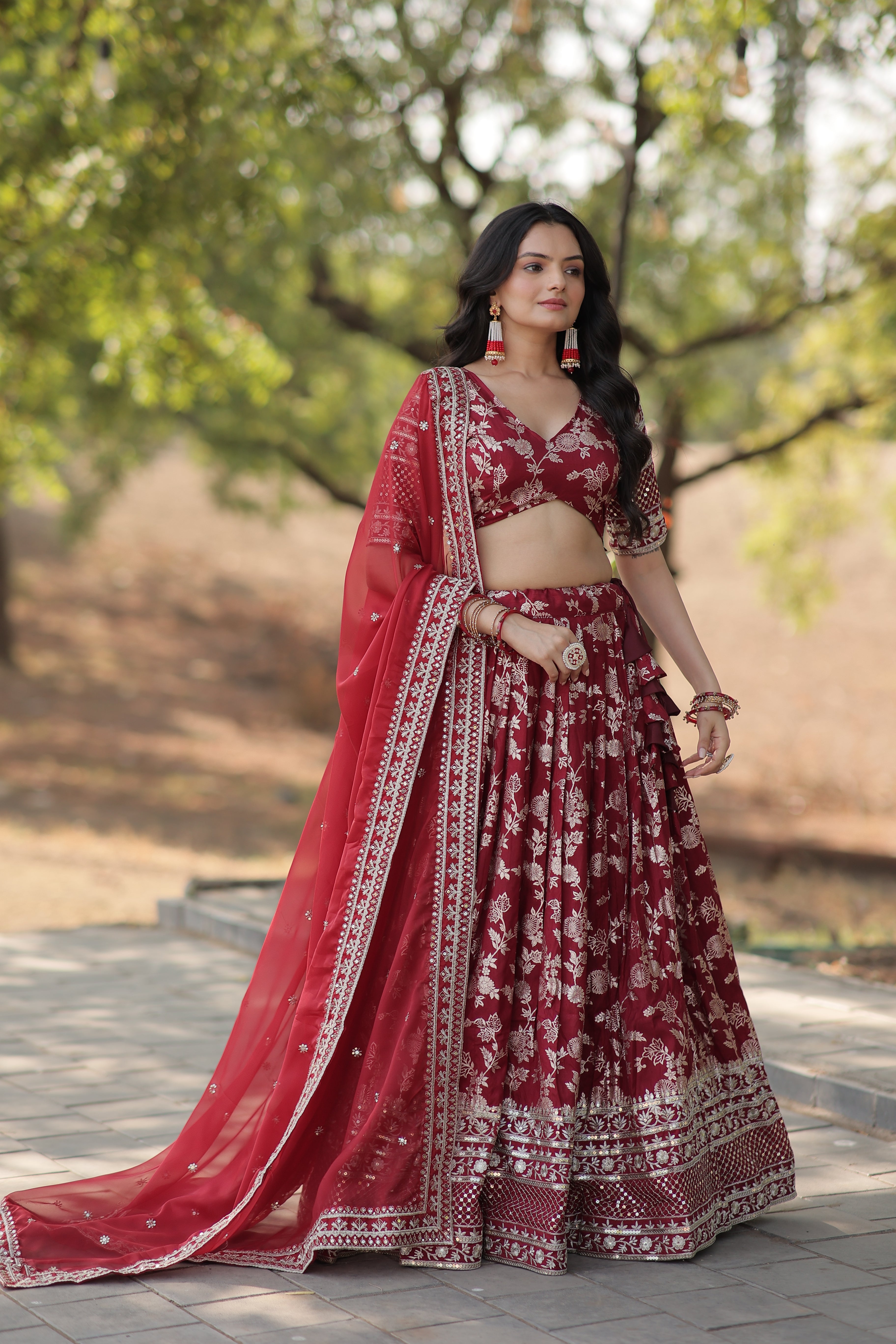 Woman in a red traditional outfit standing outdoors with trees in the background