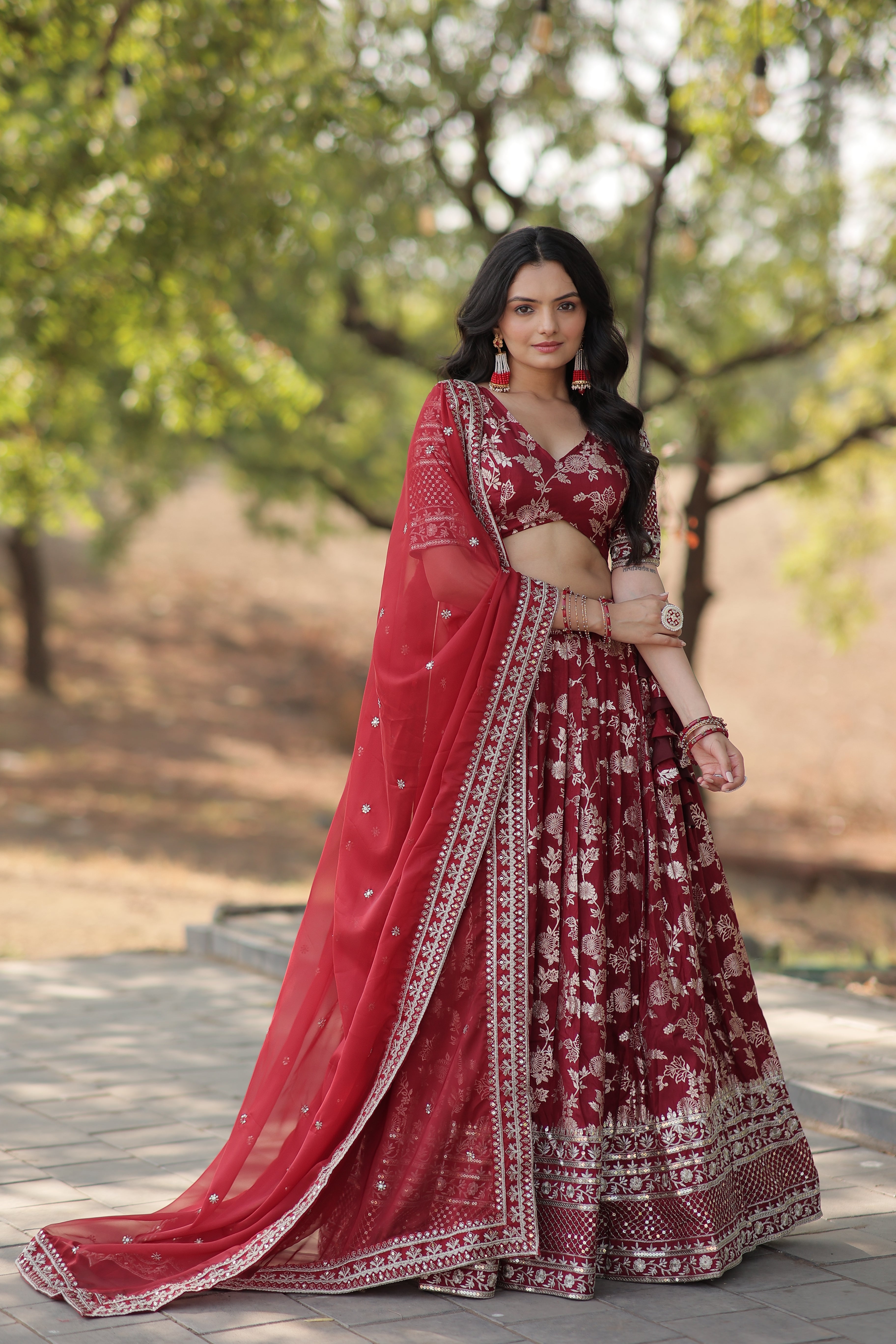 Woman in a red and white traditional outfit standing outdoors with trees in the background