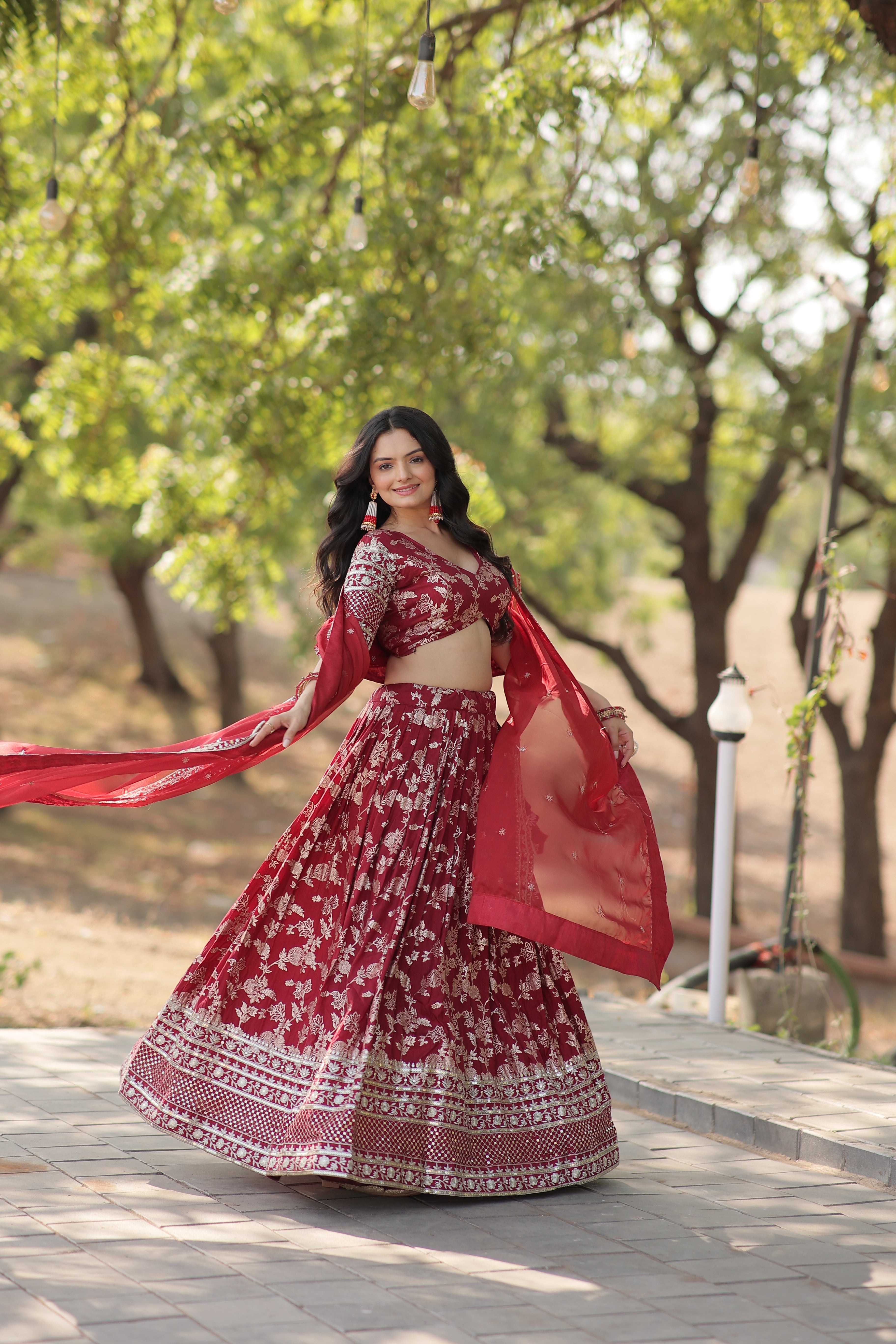 Woman in a red traditional outfit standing against a tree with greenery in the background