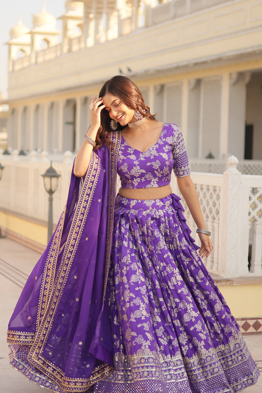 Woman wearing a purple traditional outfit with white patterns in an indoor setting.
