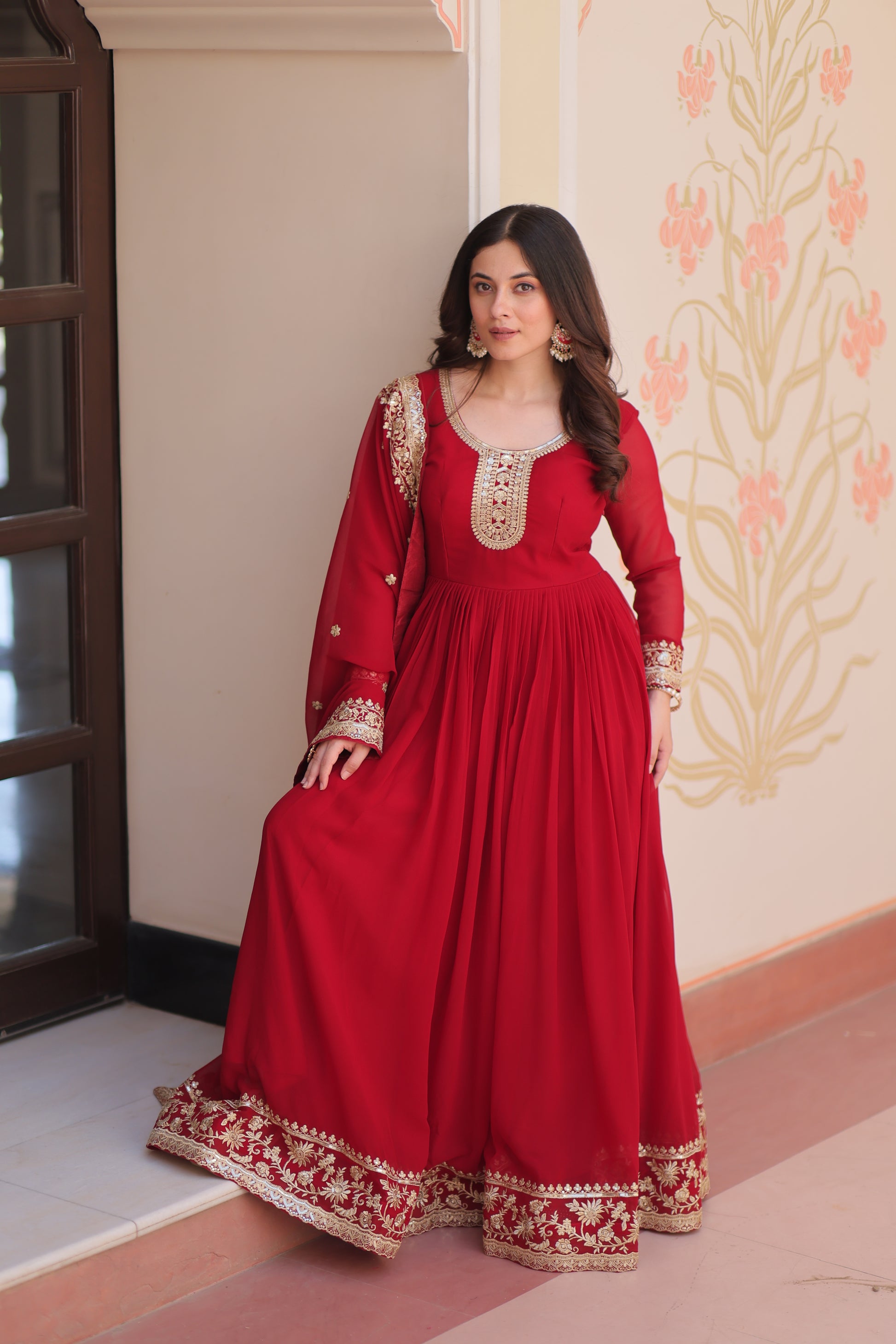 Woman wearing a red traditional outfit with gold embroidery in a room.