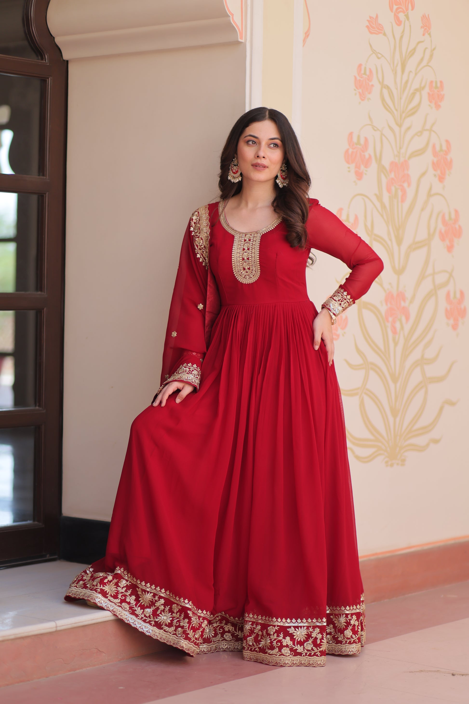 Woman wearing a red traditional outfit with white embroidery indoors.