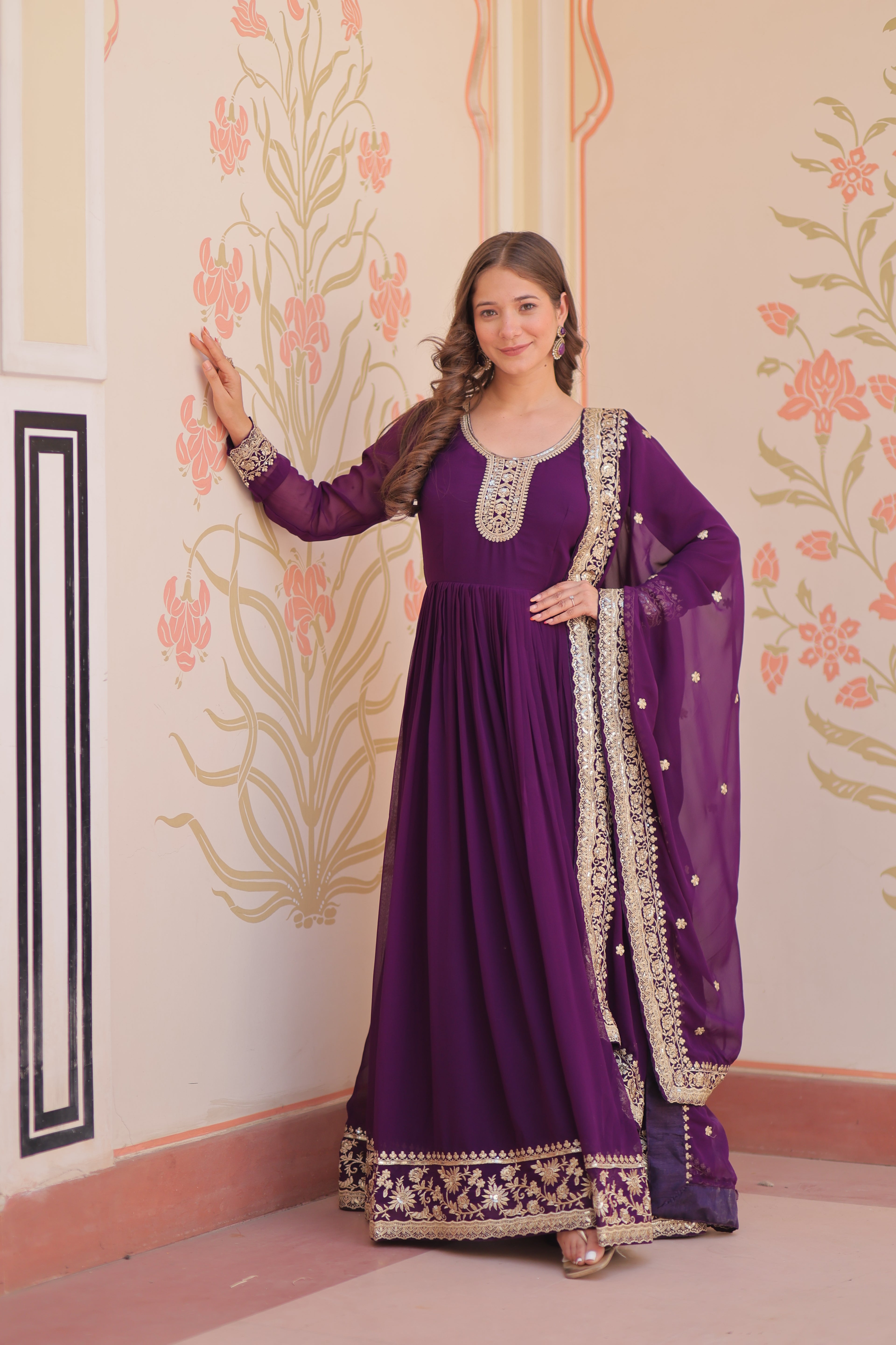 Woman wearing a purple traditional outfit with intricate designs in a decorated room.