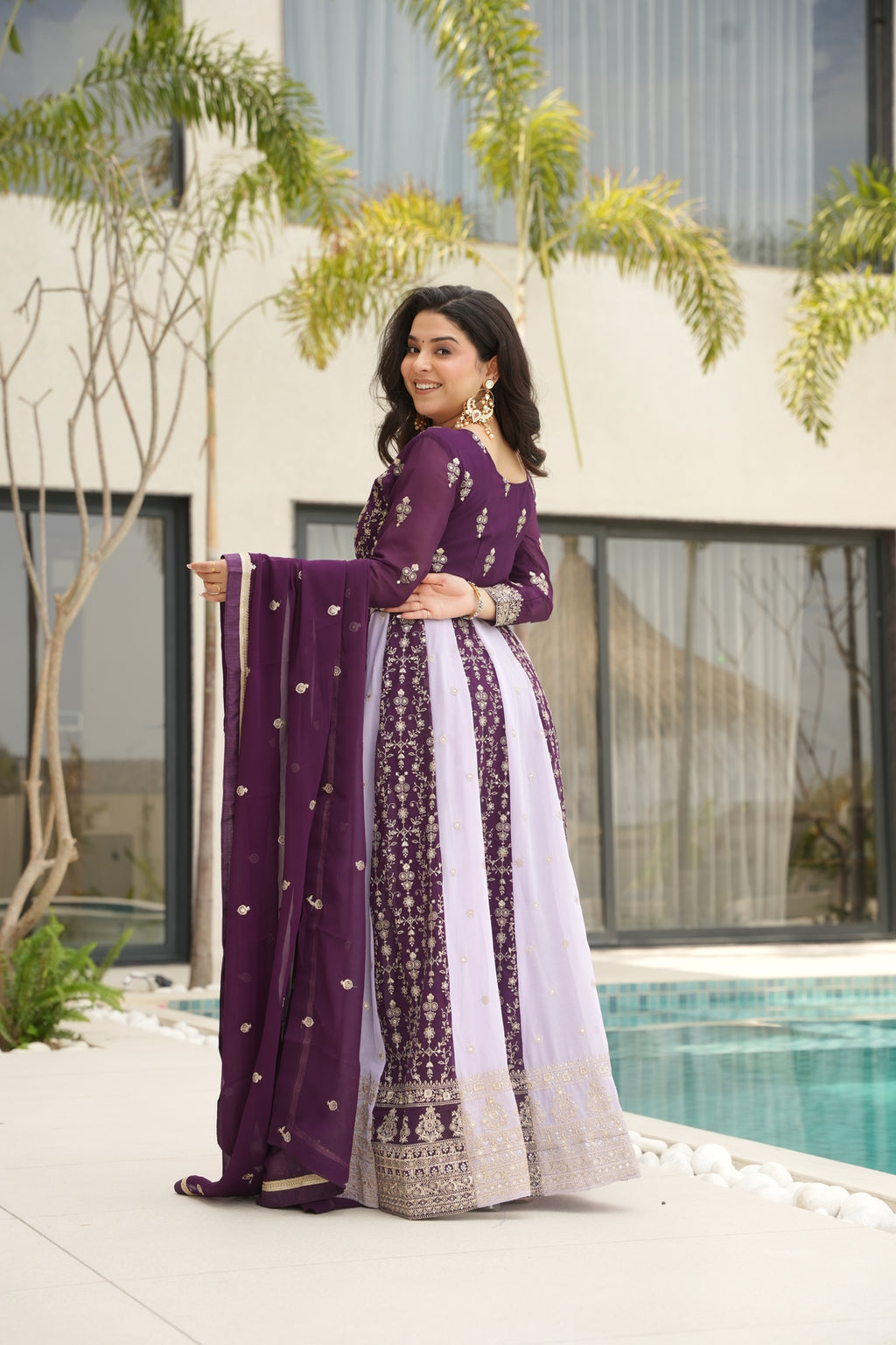 Woman wearing a purple traditional outfit with a white dupatta, standing outdoors.