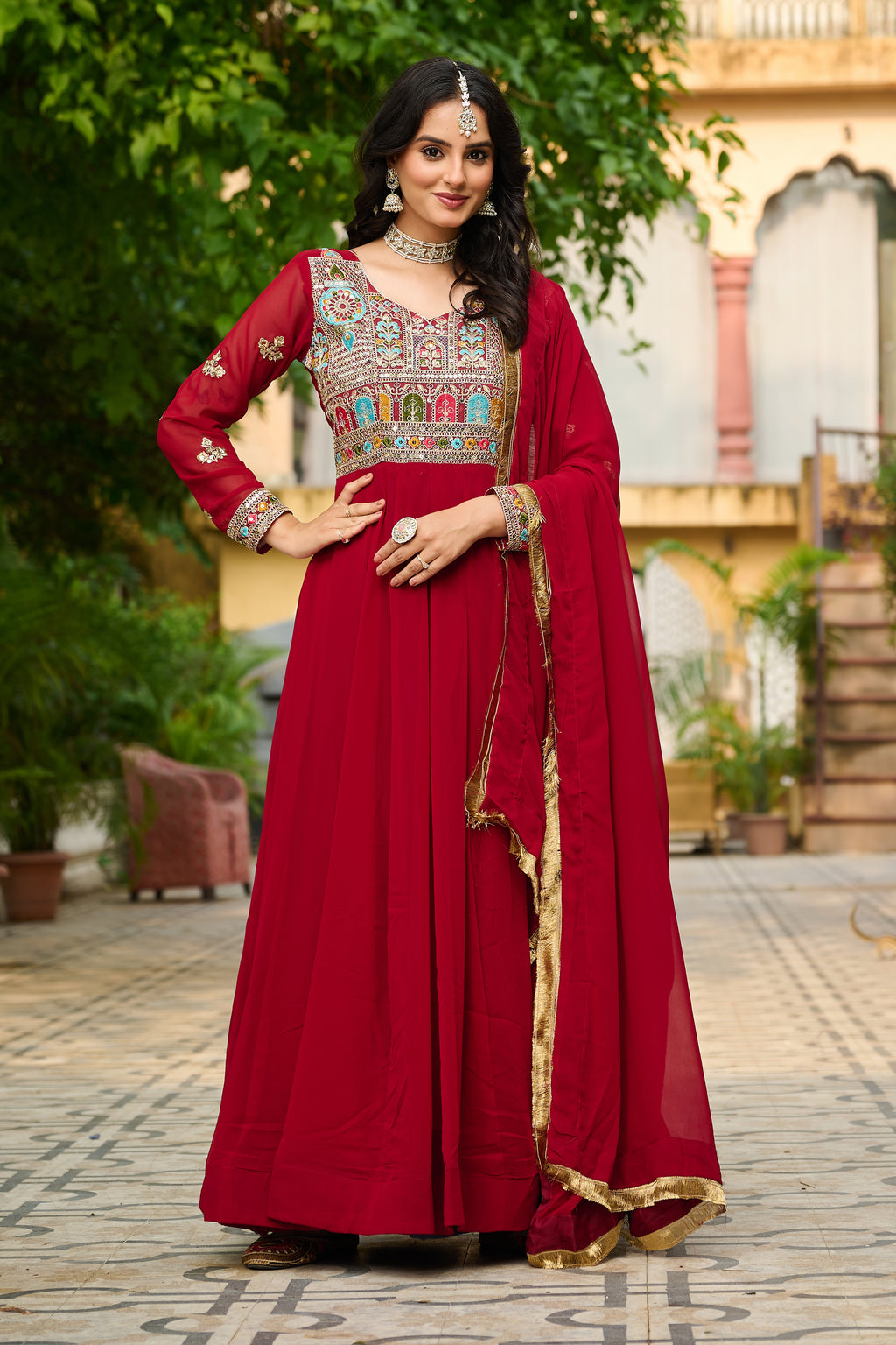 Woman in a red traditional outfit with intricate patterns standing outdoors.