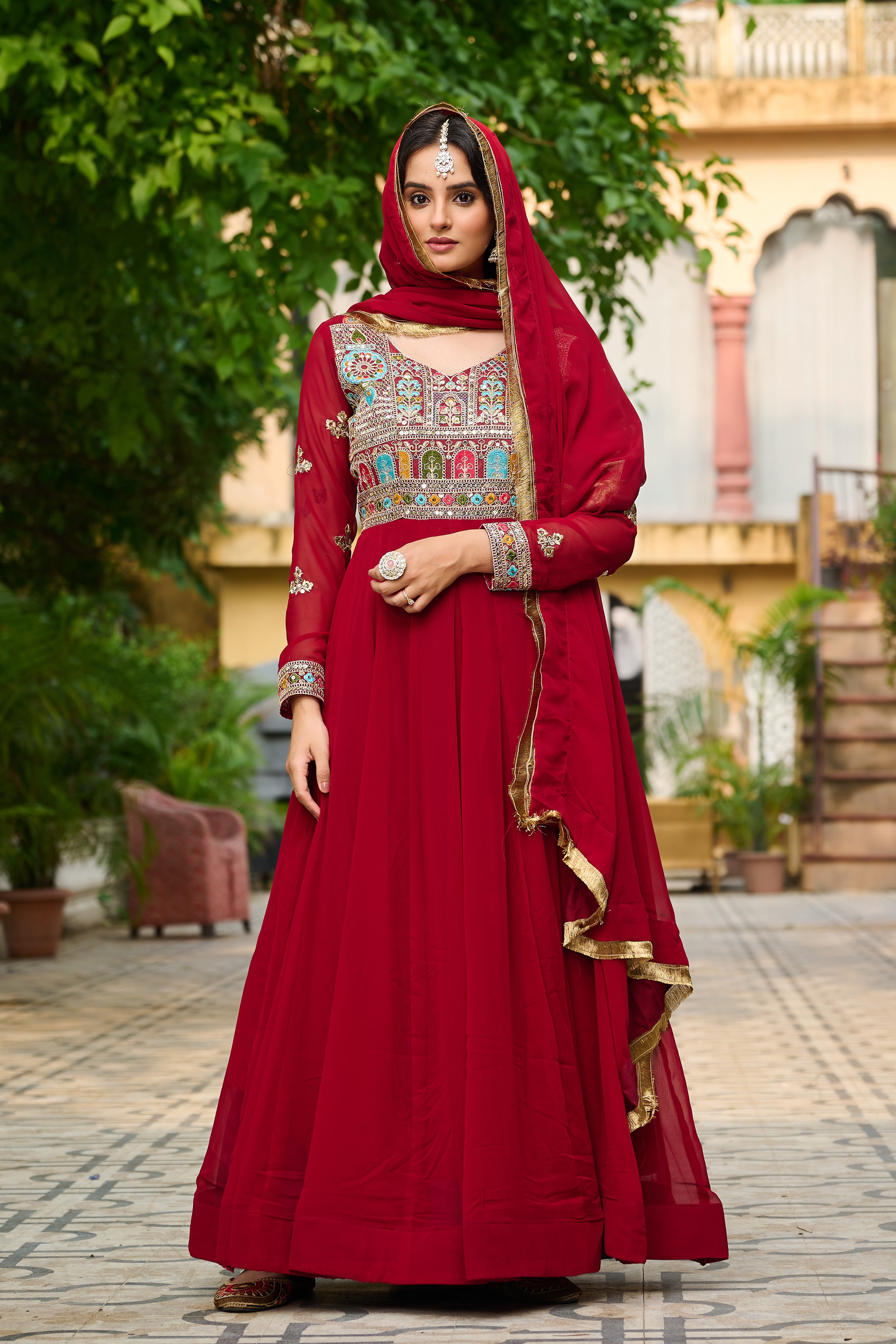Woman in a red traditional outfit with intricate patterns standing outdoors.