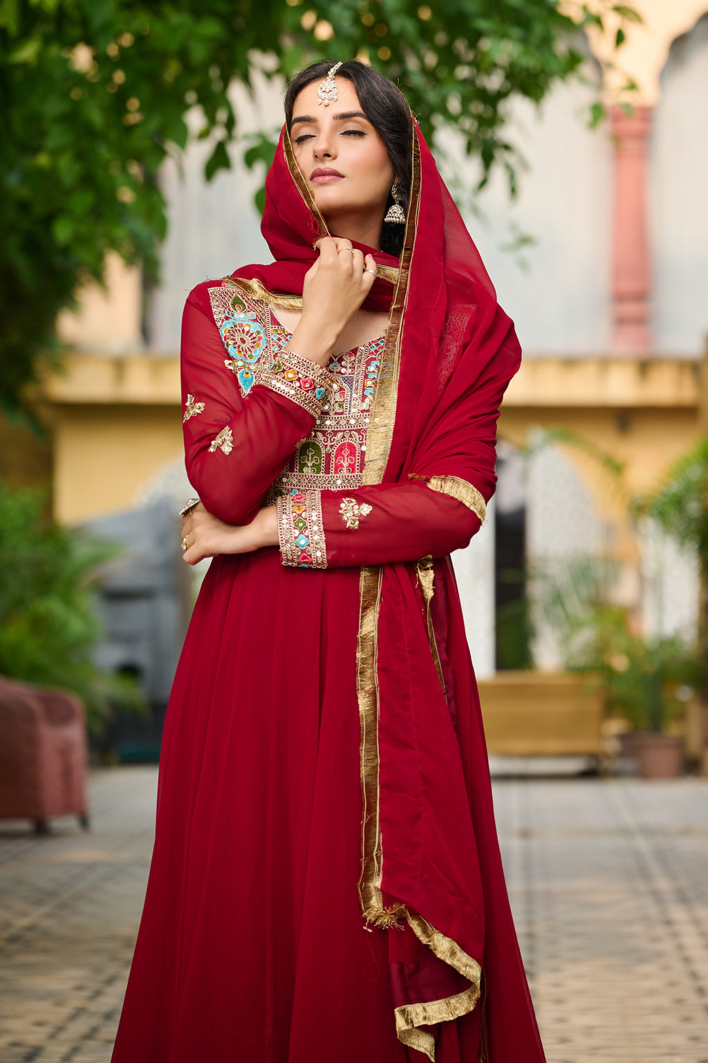 Woman in a red traditional outfit with gold details outdoors.